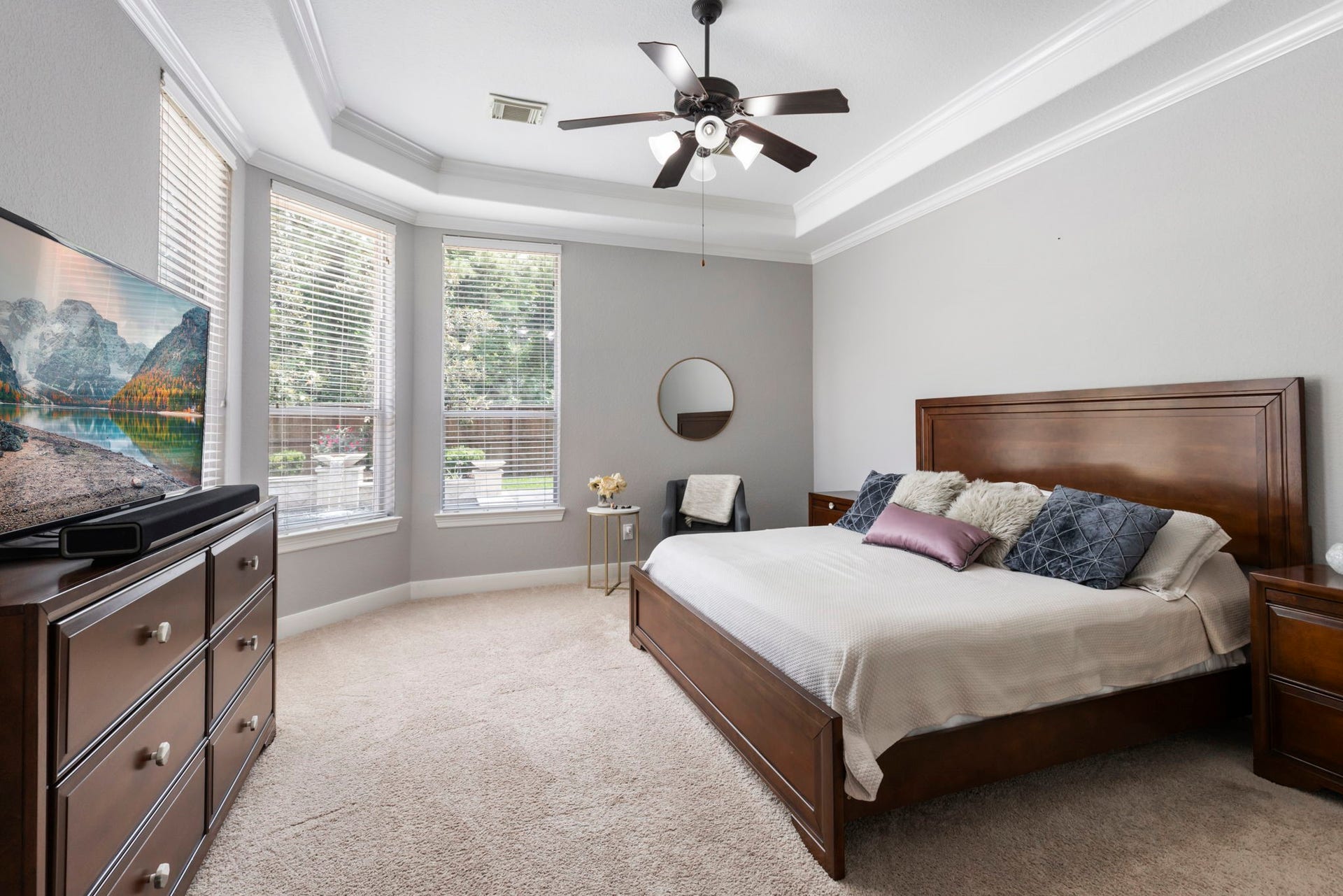 130 S Arrow Canyon Circle, The Woodlands, TX 77389 This spacious bedroom features large windows for natural light and a tray ceiling with a fan. The neutral wall color and soft carpet add a cozy feel, perfect for relaxation.