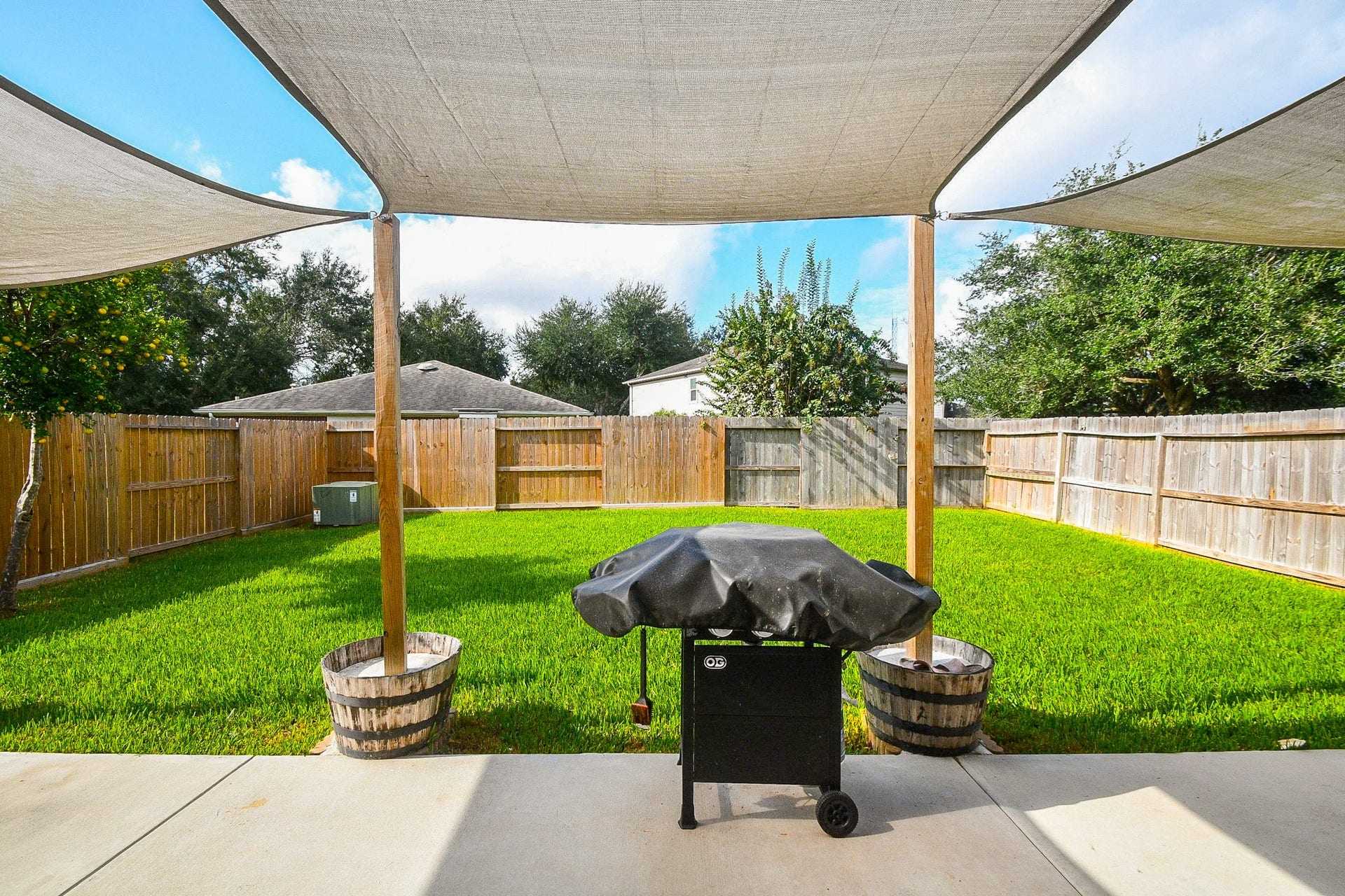 10222 Antelope Alley, Missouri City, TX 77459 Spacious backyard retreat features lush green lawn, shaded patio with sail canopies, and a barbecue grill, perfect for outdoor entertaining.