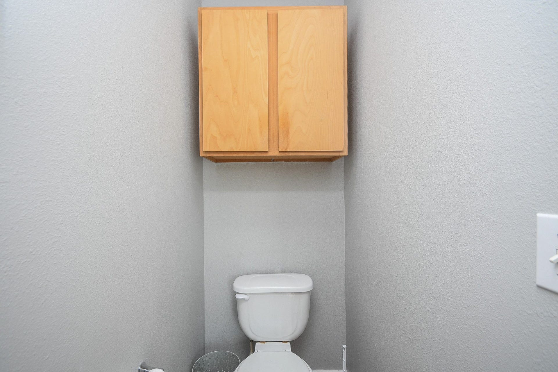 10222 Antelope Alley, Missouri City, TX 77459 Compact bathroom featuring a modern toilet and overhead storage cabinet, set against neutral gray walls.