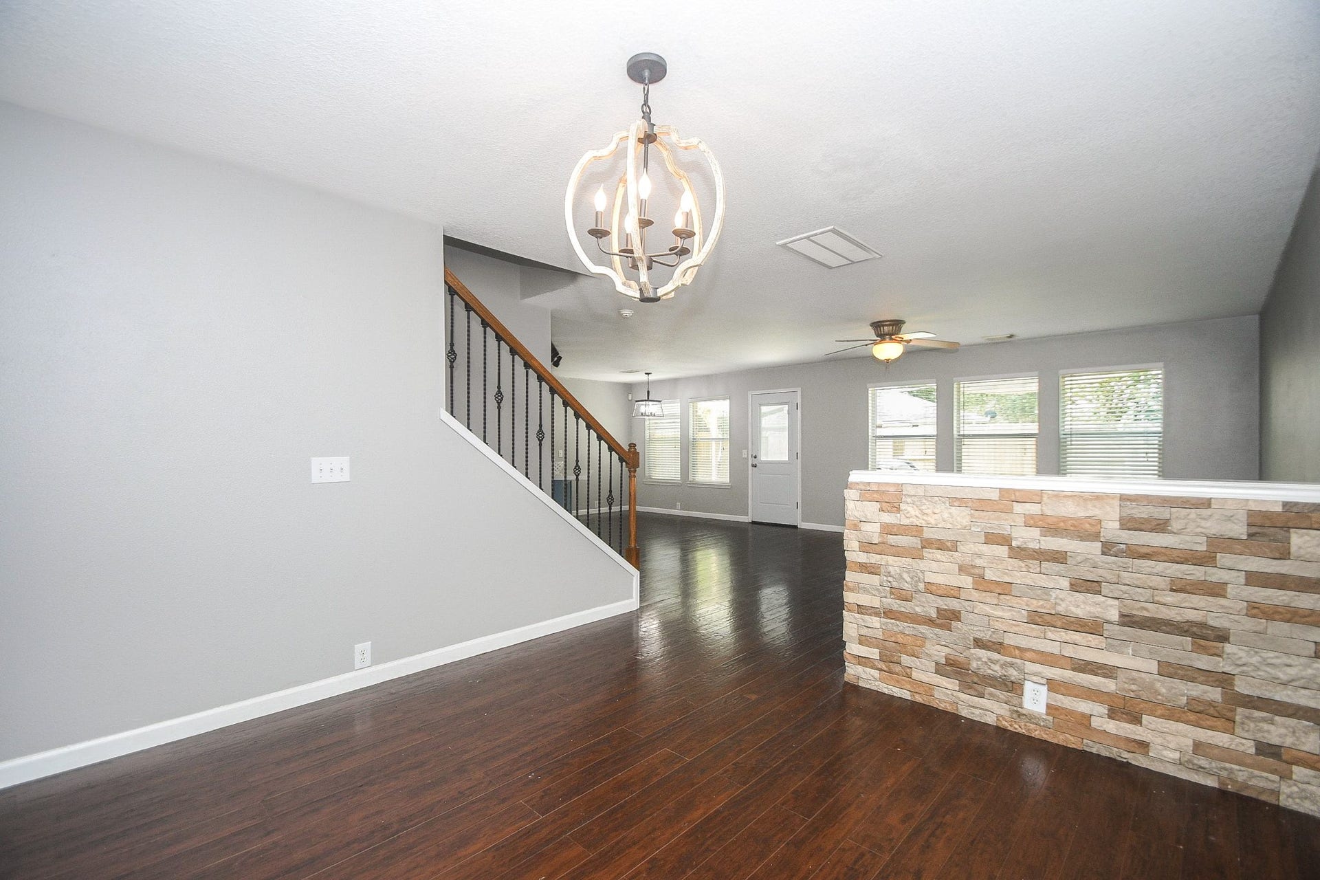 10222 Antelope Alley, Missouri City, TX 77459 Spacious open-concept living area features elegant laminate wood floors, a modern light fixture, and a stylish stone accent wall, leading to a staircase with wrought iron railings.