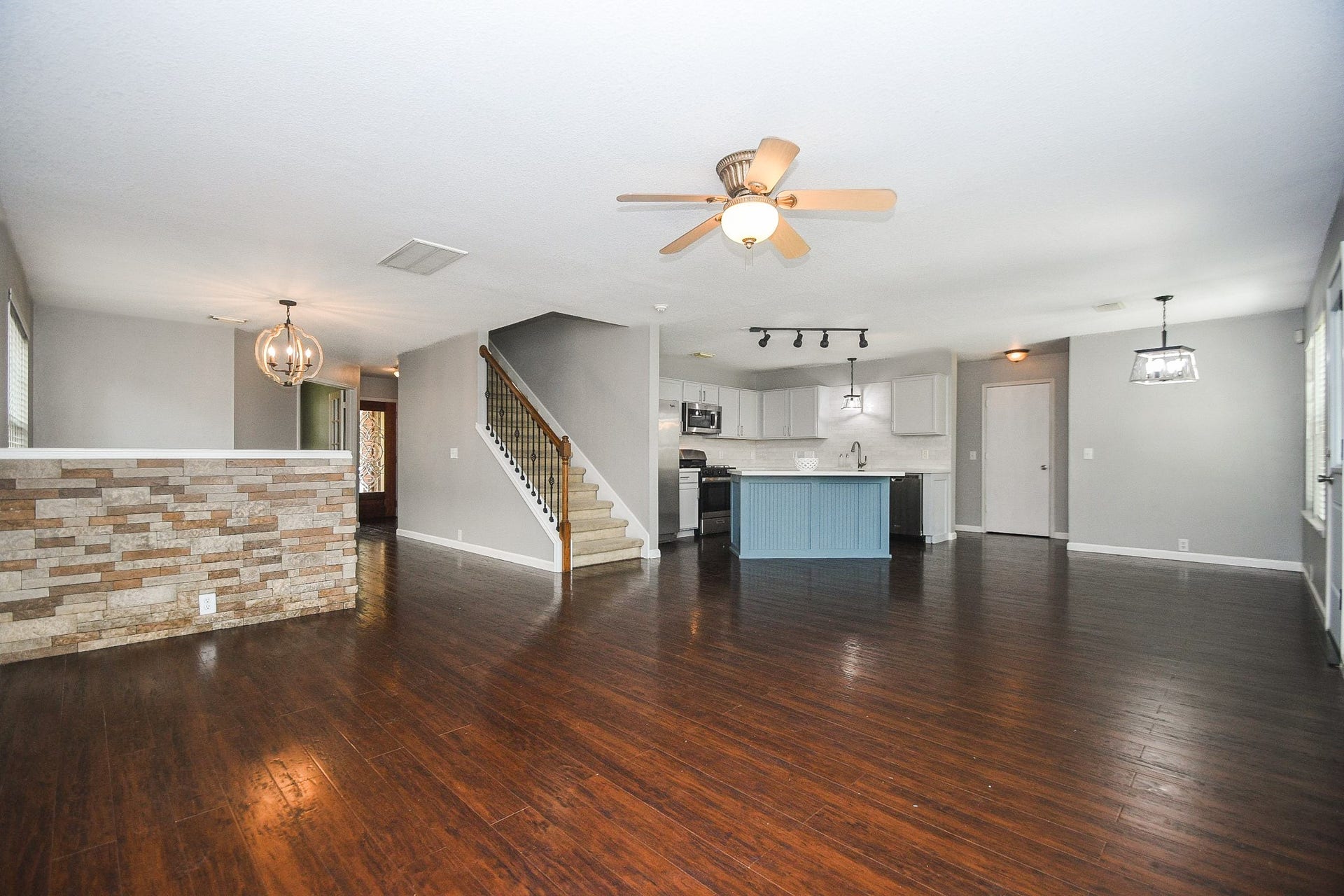 10222 Antelope Alley, Missouri City, TX 77459 Spacious open-concept living area with rich hardwood floors, a modern kitchen featuring a stylish blue island, and elegant lighting fixtures. The space includes a cozy dining area and a staircase with wrought iron railing, perfect for both entertaining and everyday living.