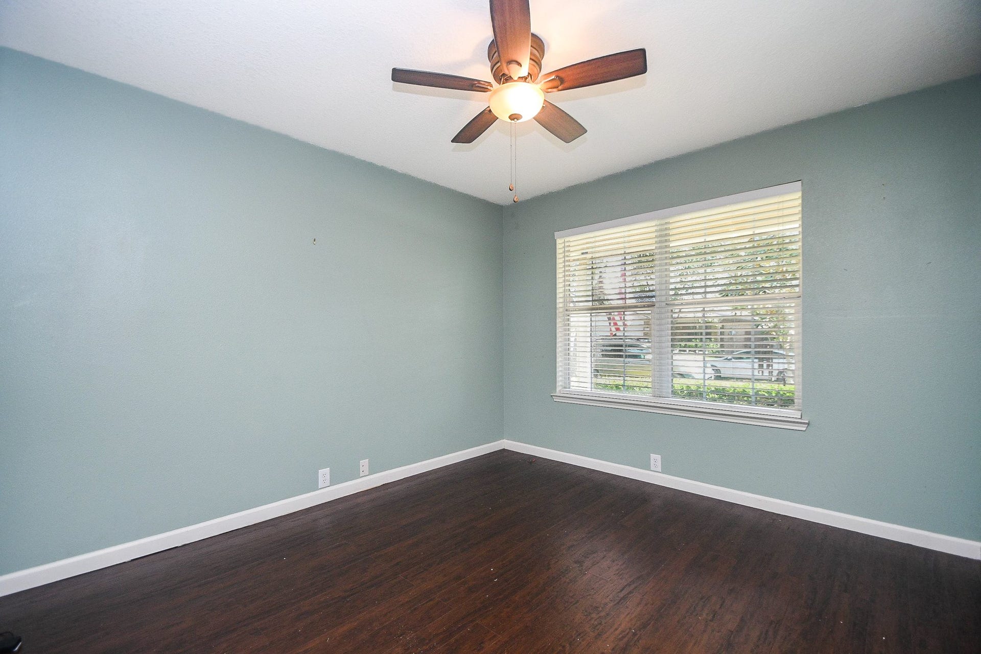 10222 Antelope Alley, Missouri City, TX 77459 Spacious home office/study with rich, laminate wood flooring, a soothing blue accent wall, and ample natural light from a large window, complemented by a modern ceiling fan.