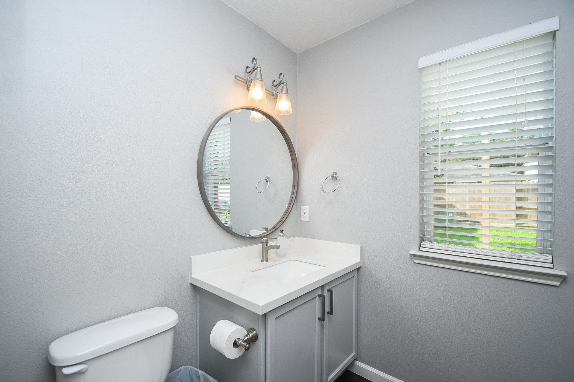 10222 Antelope Alley, Missouri City, TX 77459 Bright and modern bathroom featuring a sleek vanity with a round mirror, complemented by soft lighting and a window for natural light.