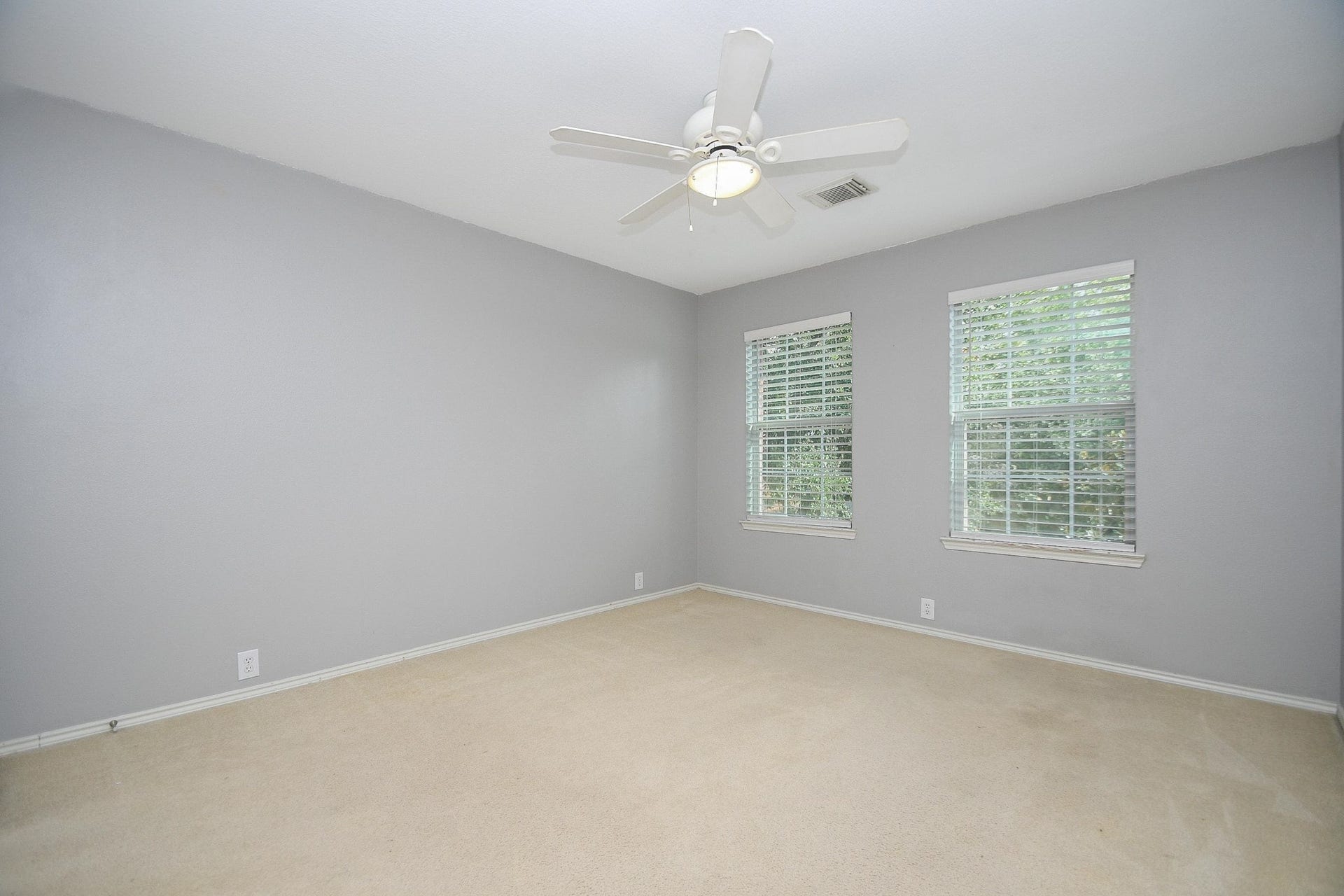 10222 Antelope Alley, Missouri City, TX 77459 Spacious bedroom with soft gray walls, plush carpeting, and ample natural light from two large windows, complete with a ceiling fan for comfort.