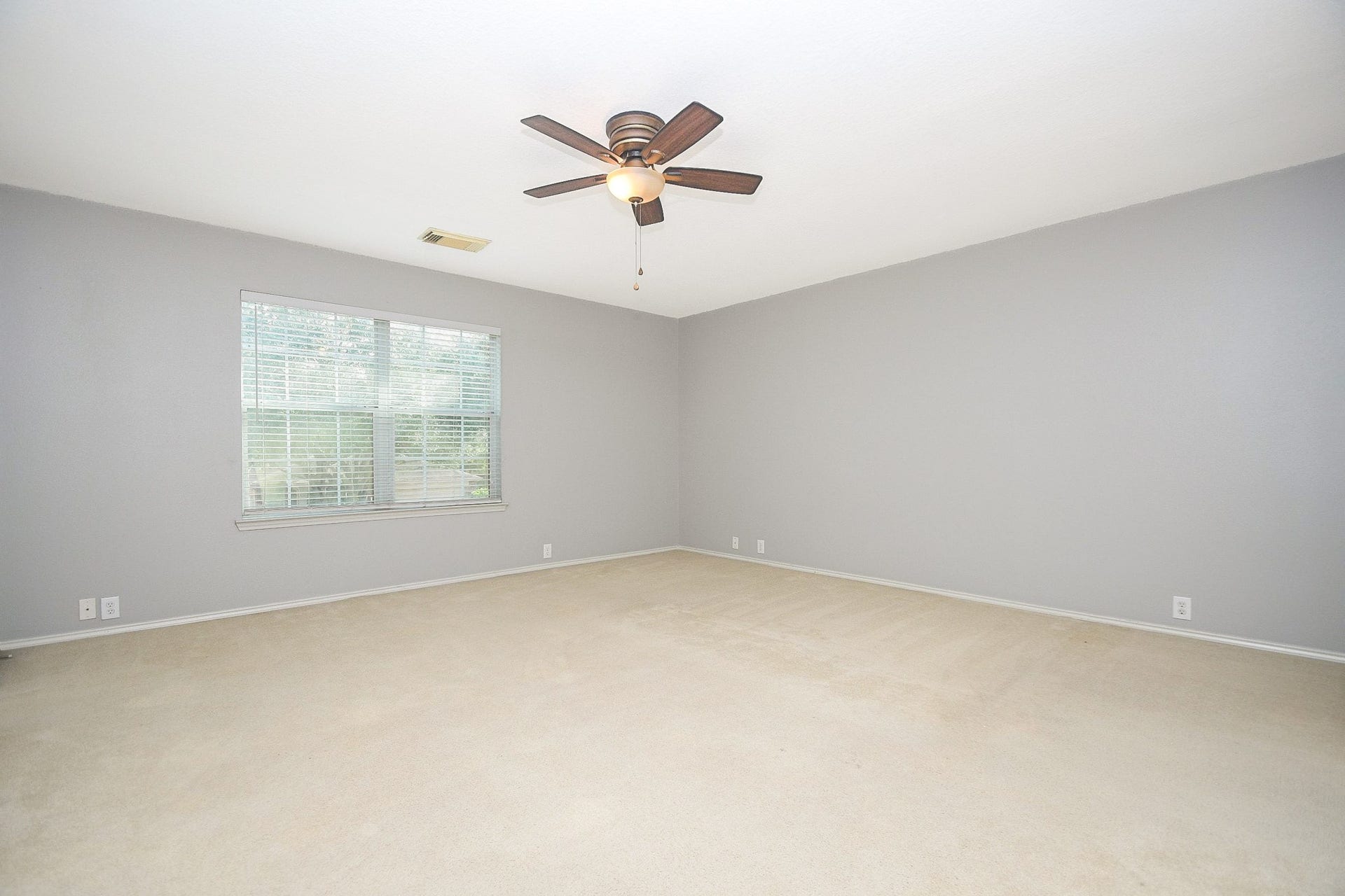 10222 Antelope Alley, Missouri City, TX 77459 Spacious bedroom with soft carpet, neutral gray walls, and a ceiling fan, offering ample natural light through a large window.