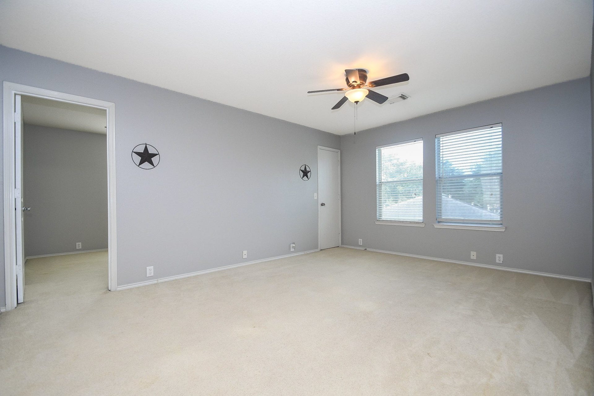 10222 Antelope Alley, Missouri City, TX 77459 Spacious bedroom with soft carpet, neutral gray walls, and ample natural light from two large windows, complemented by a ceiling fan for comfort.