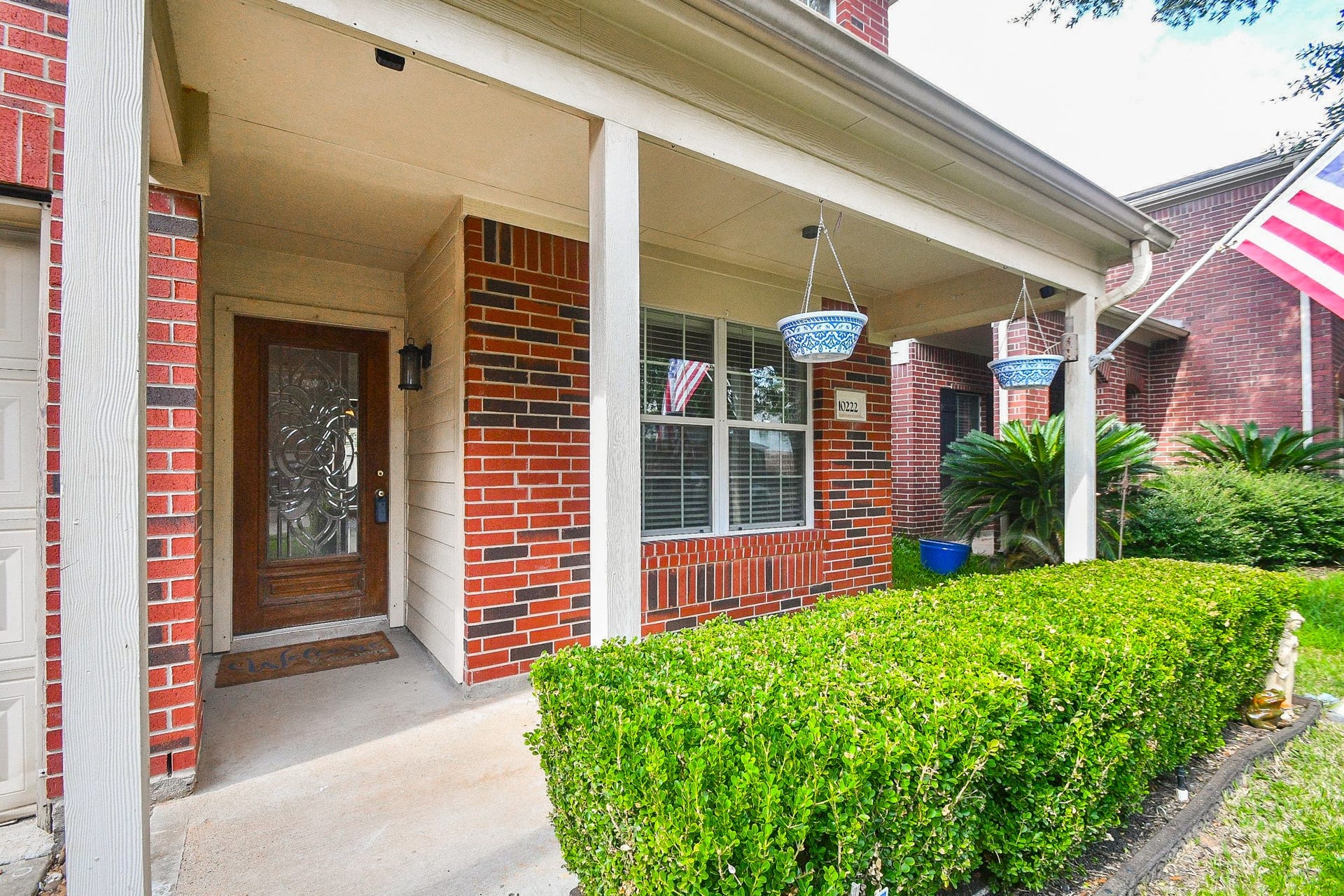 10222 Antelope Alley, Missouri City, TX 77459 Charming brick home with a welcoming front porch, decorative glass door, and lush greenery, perfect for relaxing outdoors.