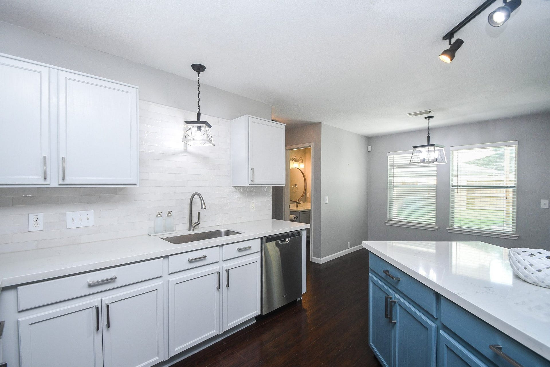 10222 Antelope Alley, Missouri City, TX 77459 Bright kitchen featuring modern white cabinetry, sleek stainless steel appliances, and a stylish island with blue accents, complemented by dark hardwood floors and ample natural light.