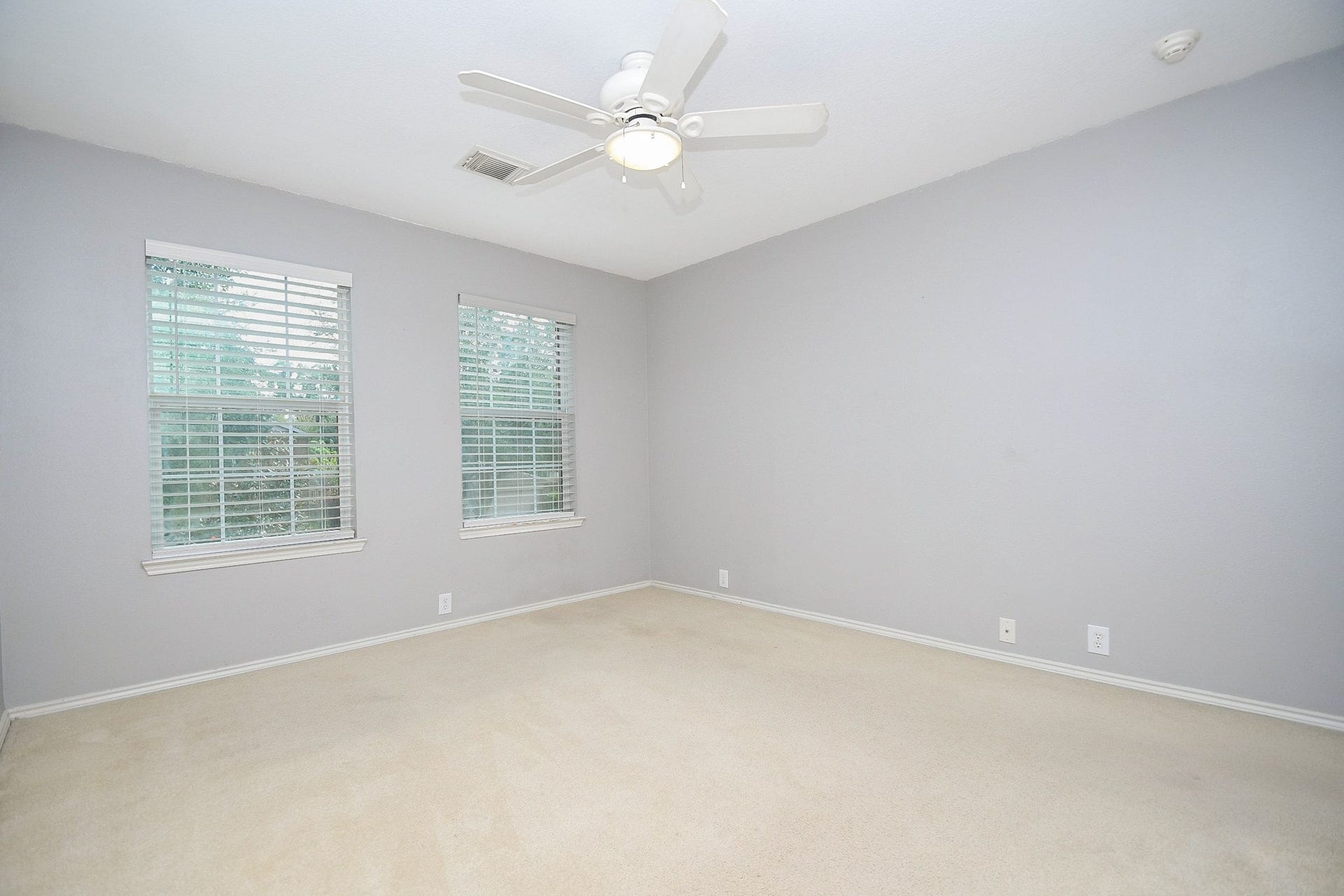 10222 Antelope Alley, Missouri City, TX 77459 Spacious room with soft gray walls, plush carpeting, and ample natural light from two large windows, complete with a ceiling fan for comfort.