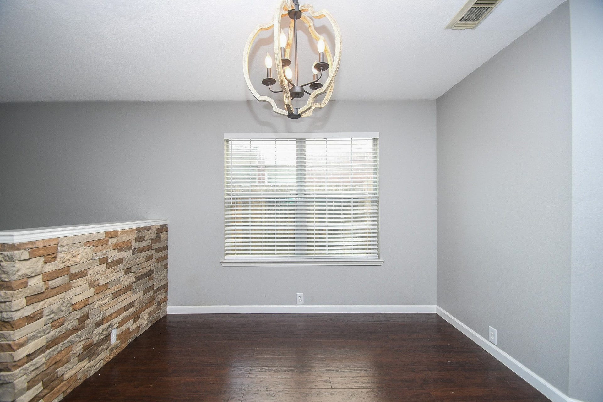 10222 Antelope Alley, Missouri City, TX 77459 Charming room featuring a modern chandelier, rich dark wood flooring, and a stylish stone accent wall, creating an inviting atmosphere.
