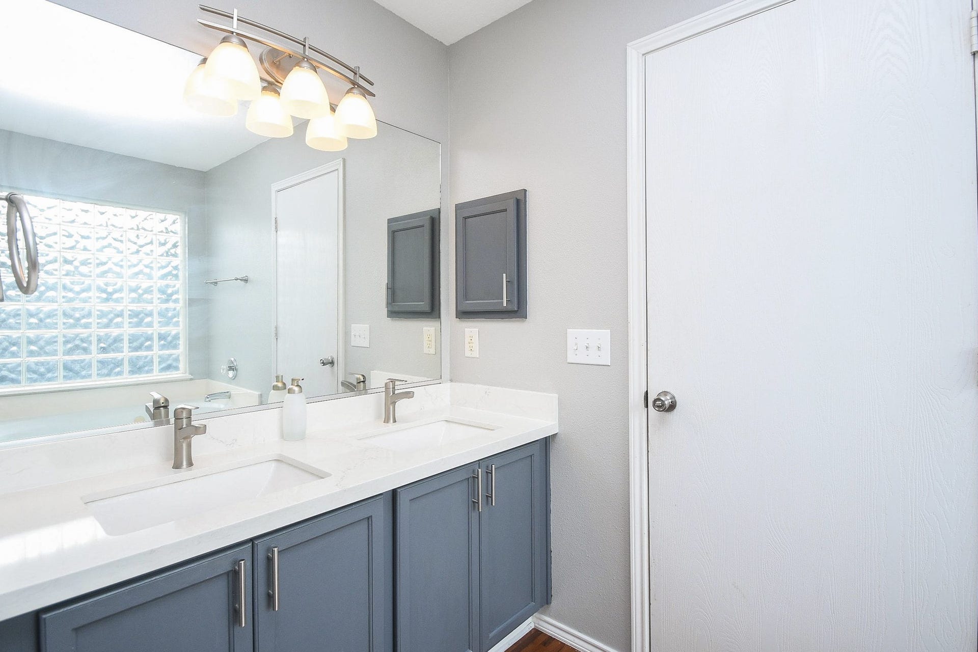 10222 Antelope Alley, Missouri City, TX 77459 Elegant bathroom featuring a double vanity with sleek faucets, modern lighting, and ample cabinet storage, complemented by a stylish glass block window for natural light.