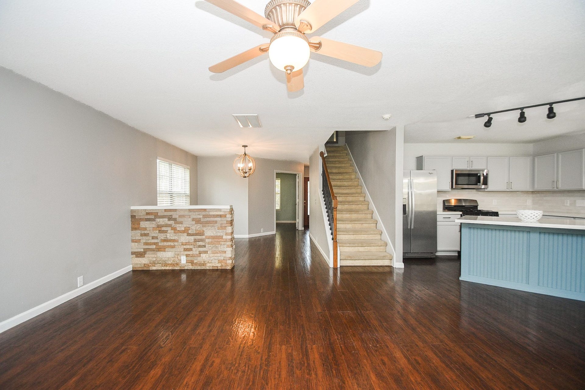 10222 Antelope Alley, Missouri City, TX 77459 Spacious open-concept living area with rich wood floors, modern kitchen featuring stainless steel appliances, and a stylish breakfast bar, all complemented by a cozy brick accent wall.