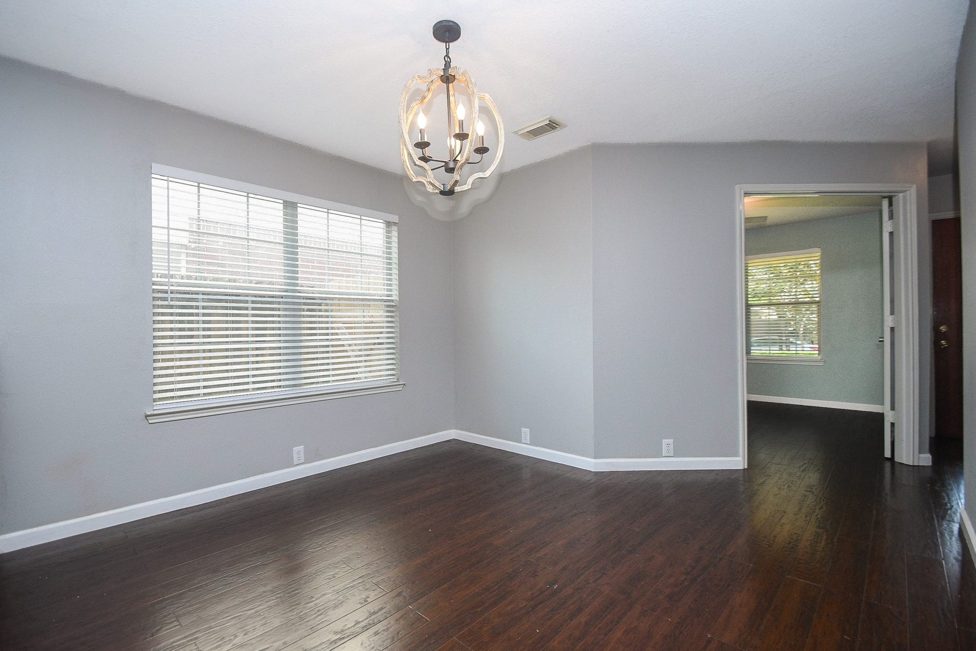 10222 Antelope Alley, Missouri City, TX 77459 Bright and inviting room featuring rich hardwood floors, a modern chandelier, and ample natural light from large windows, with a doorway leading to an adjacent space.