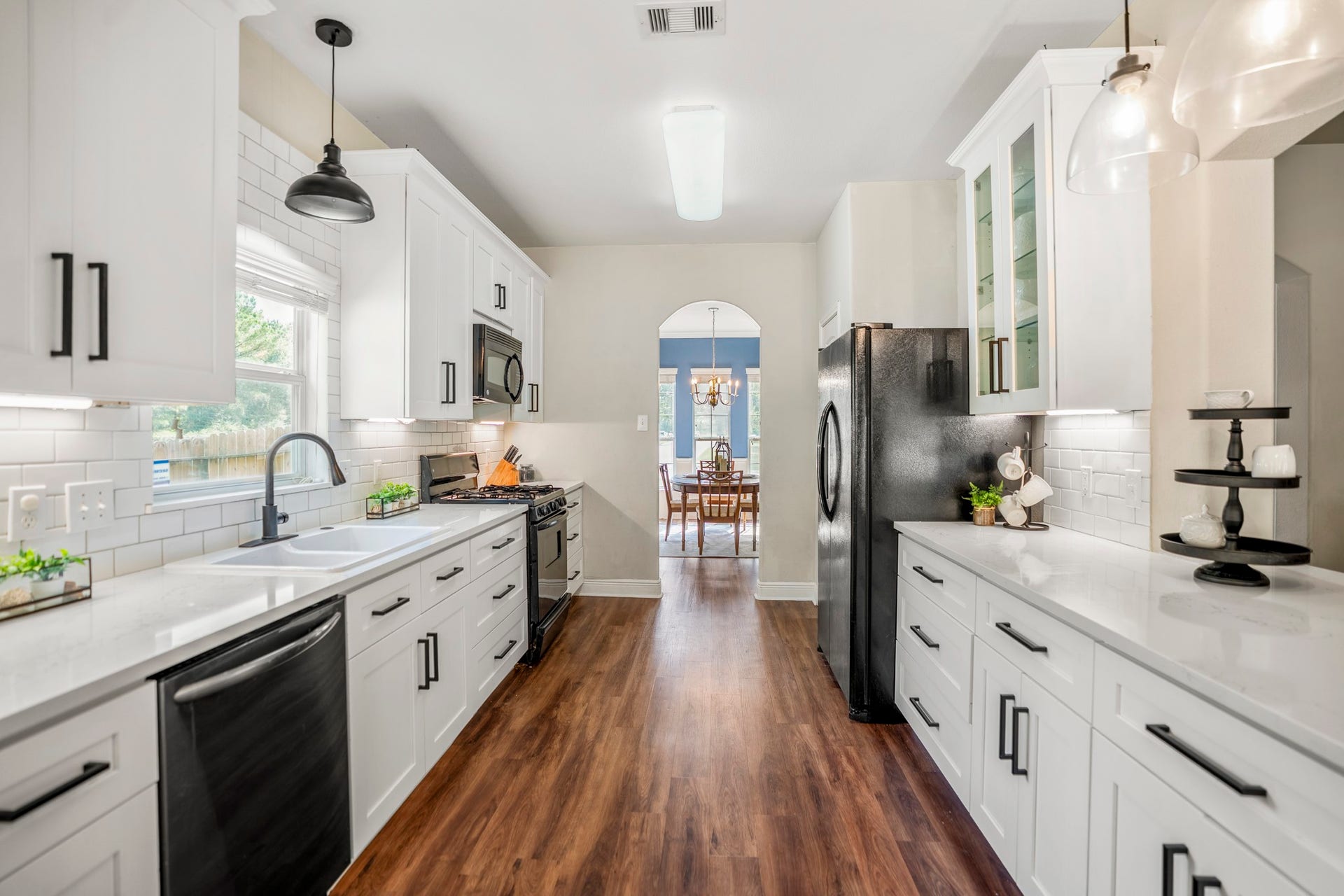 942 Oak Glen Drive, Conroe, TX 77378 Step into the remodeled kitchen, where white cabinetry, black hardware, quartz countertops, subway tile backsplash, and modern pendant lighting give the space a fresh, cohesive look. The breakfast bar was reworked as part of the remodel, opening the kitchen up for casual seating and serving, while deep drawers offer convenient storage for pots and pans. Under-cabinet lighting adds another layer of function, and the pantry door on the left keeps everyday staples close at hand.