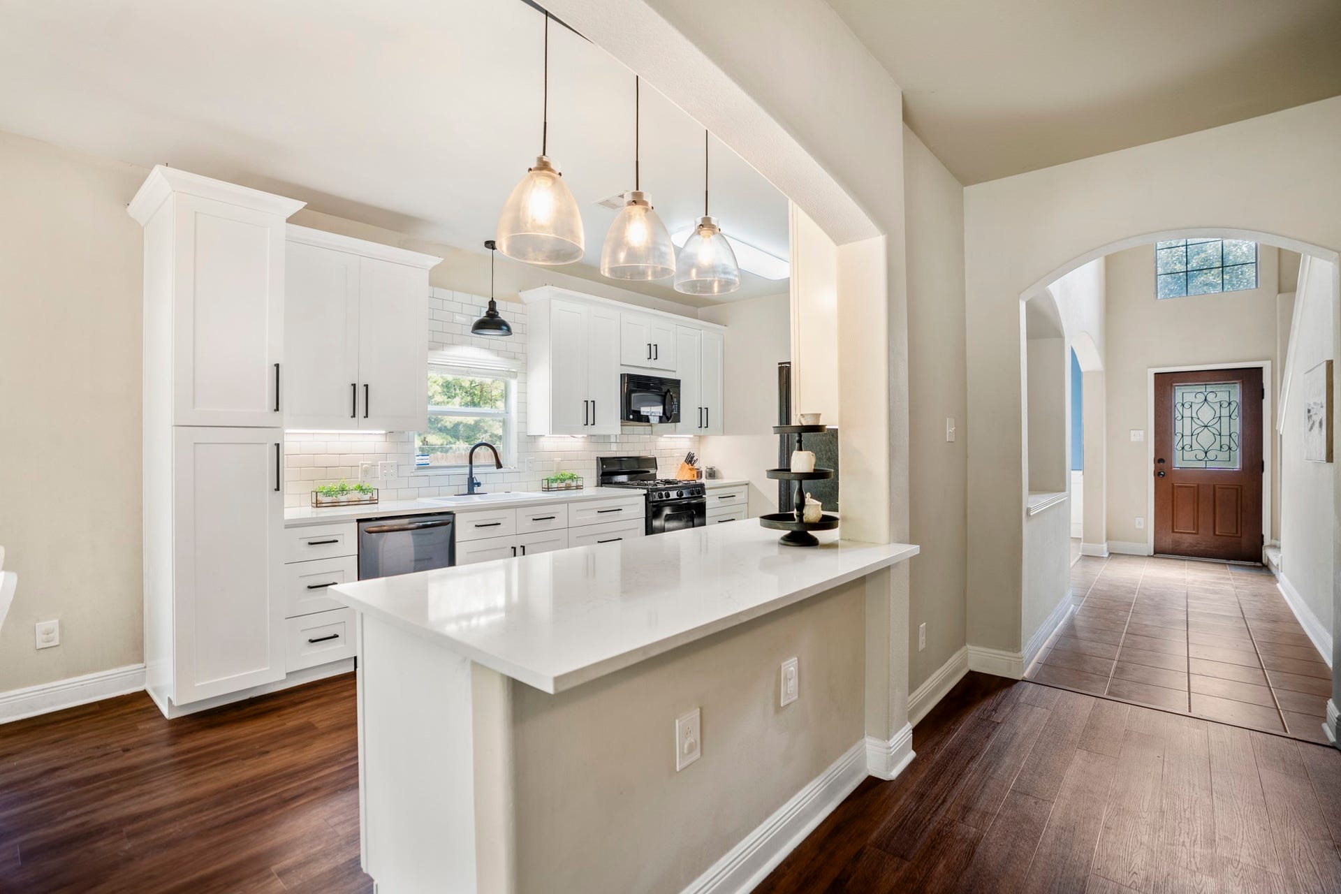942 Oak Glen Drive, Conroe, TX 77378 This angle gives you one of the best looks at the remodeled kitchen, with white cabinetry, black hardware, modern pendant lighting, and the breakfast bar opening the space up for casual seating and serving. Straight ahead, the hallway leads back toward the foyer and front of the home, while the breakfast area sits just behind and to the left of where youre standing here. Its a clean, connected layout that keeps the kitchen central to both everyday meals and entertaining.