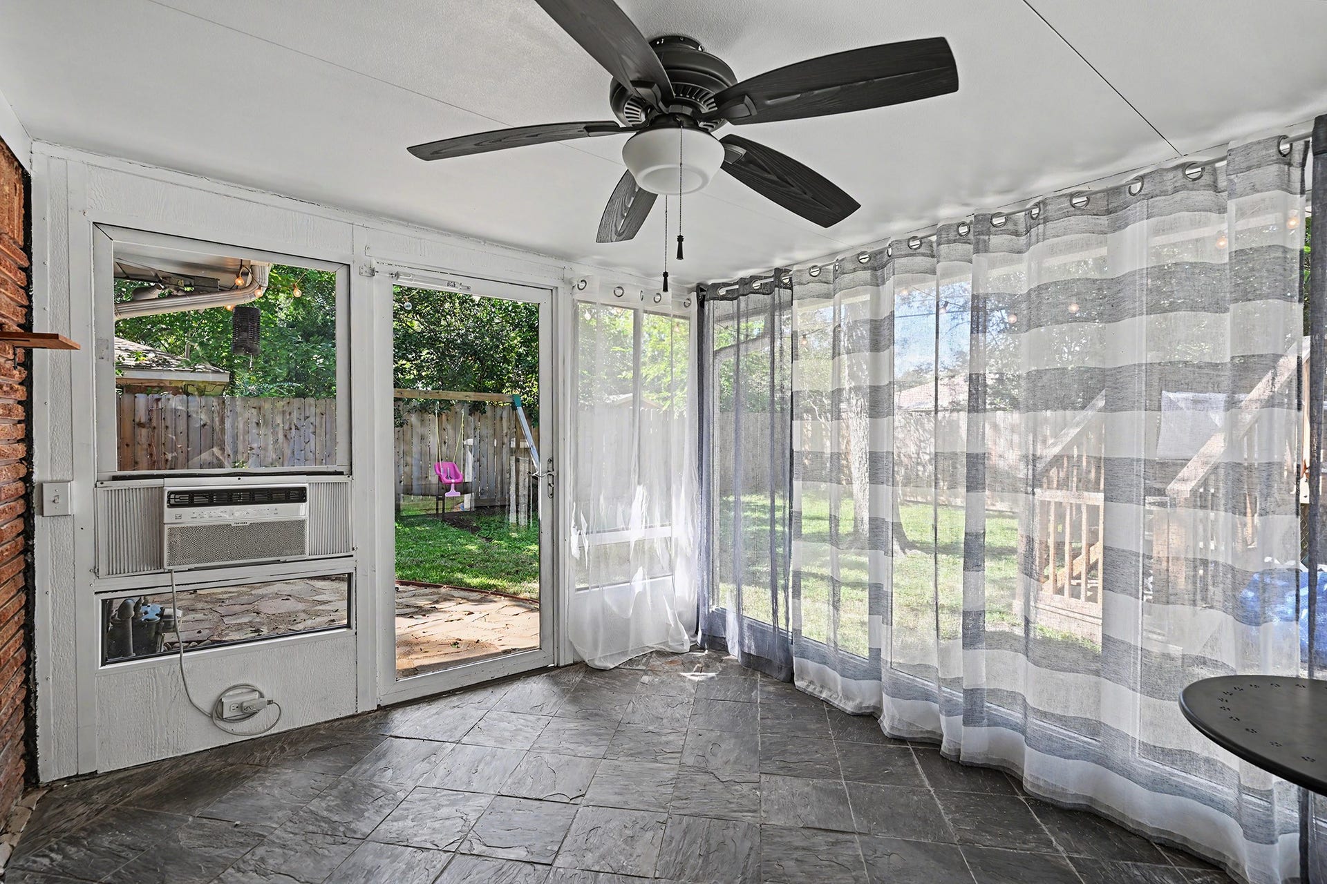 Functional and sunny closed-in porch with ceiling fan and window unit
