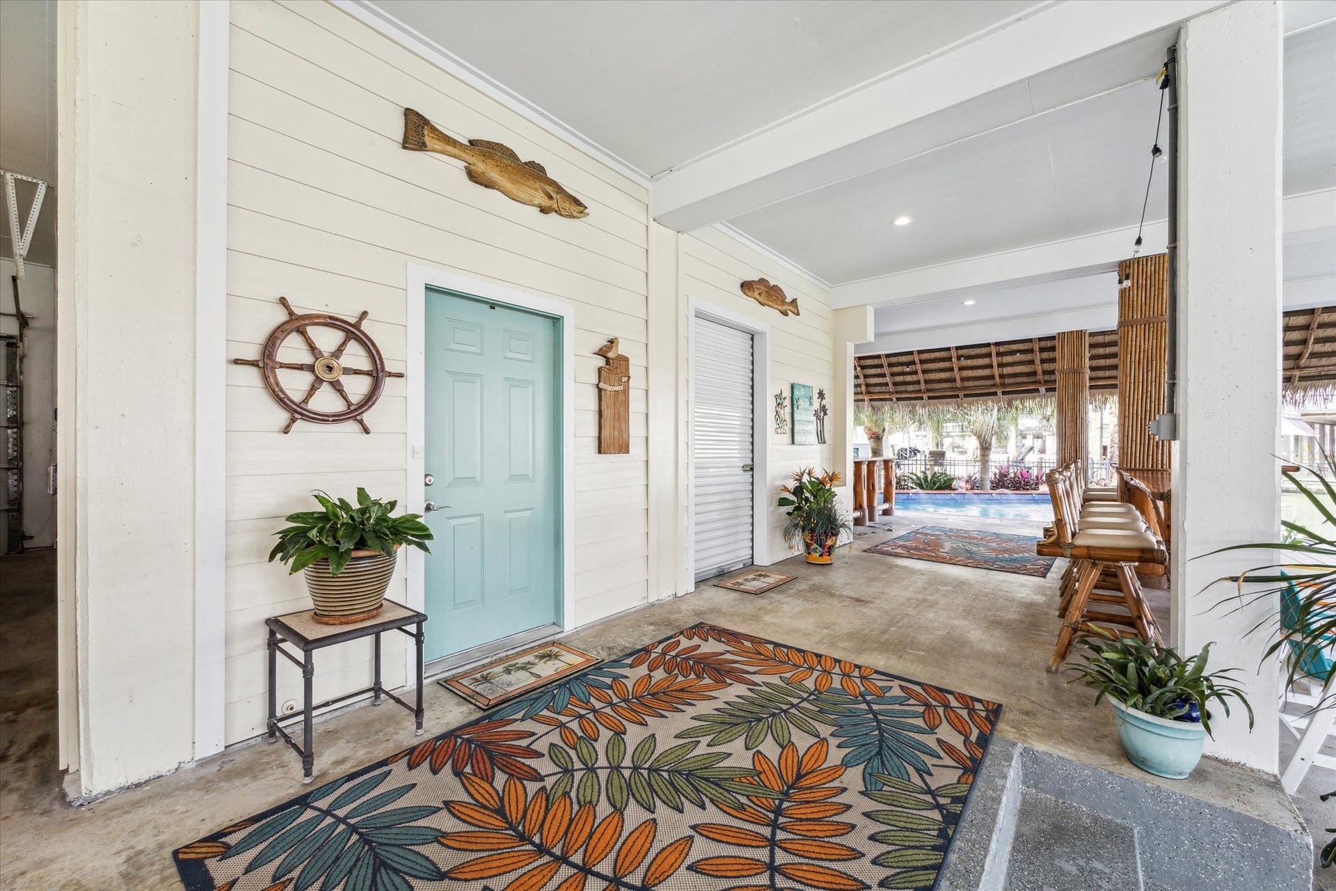 102 Bamaku Bend, Tiki Island, TX 77554 This garage level area provides an entrance into the home through the beautiful blue/green door or go through the roll up garage door to another garage space with a half bath. This patio space also has two tiki bars, access down to your 2 boat lifts or a place to sit under the palapa next to the pool. All of the bamboo has been refinished and the swivel bamboo barstool chars have been reupholstered.
