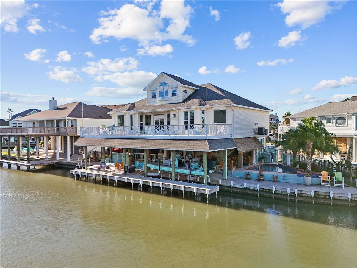 102 Bamaku Bend, Tiki Island, TX 77554 The expansive outdoor space at this home offers a raised heated pool surrounded palm trees and a covered synthetic palapa and tiki bar beside it as well as plenty of space in front of the pool to sit and enjoy the waterfront views. Below the second level deck that expands across the whole width of the home are two boat lifts (large cradle lift 33' by 10'3" and a platform lift 17' by 10'3" that can accommodate a boat lift or 2 jet skis) as well as a bait well, stainless counter space and sink & more!