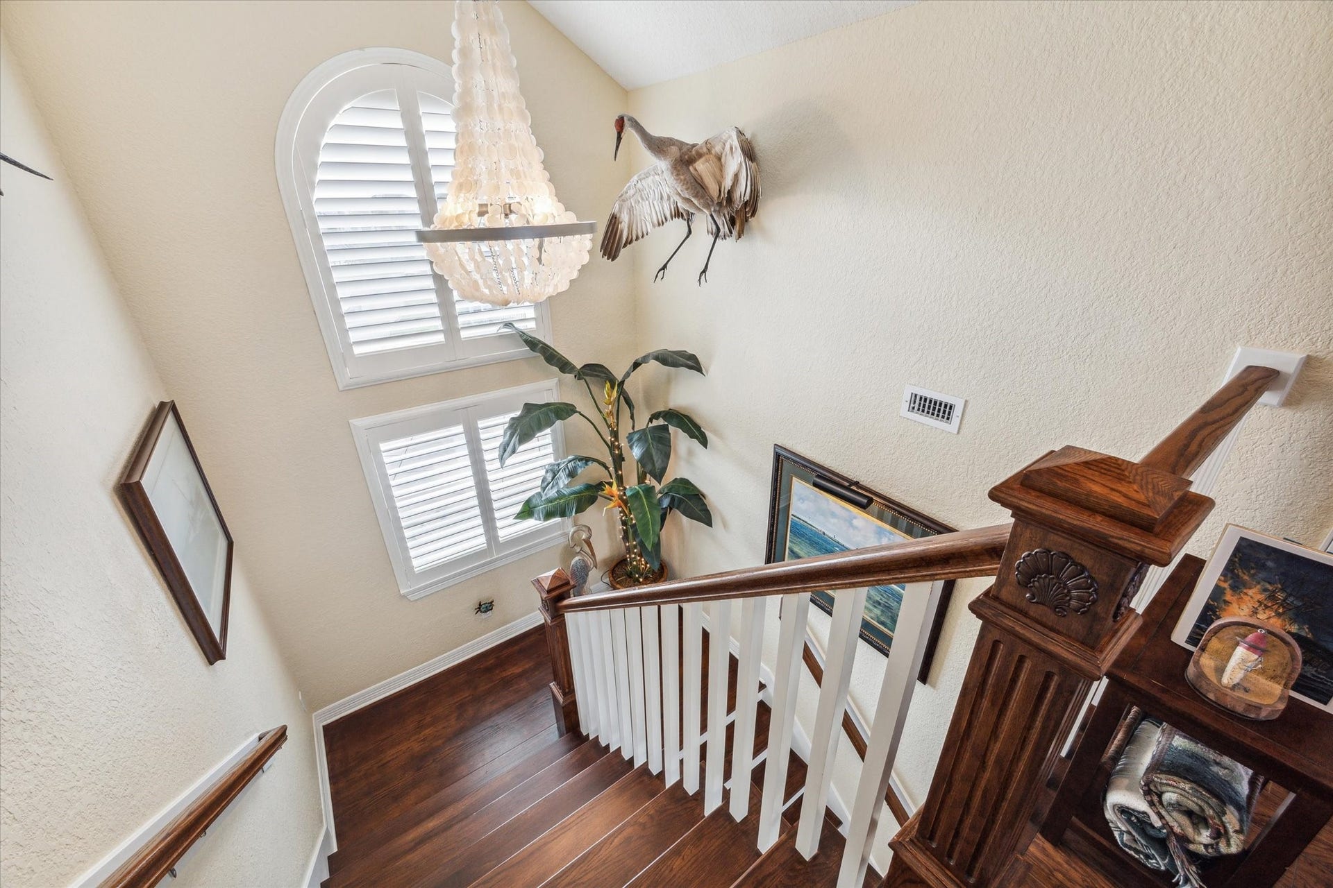 102 Bamaku Bend, Tiki Island, TX 77554 A beautiful arched window with custom plantation shutters sits at the landing going upstairs to the flex room. A beautiful chandelier adds elegance and interest to the home. In this photo you can also see the custom newel post with seashell detail. No detail was missed in this home!