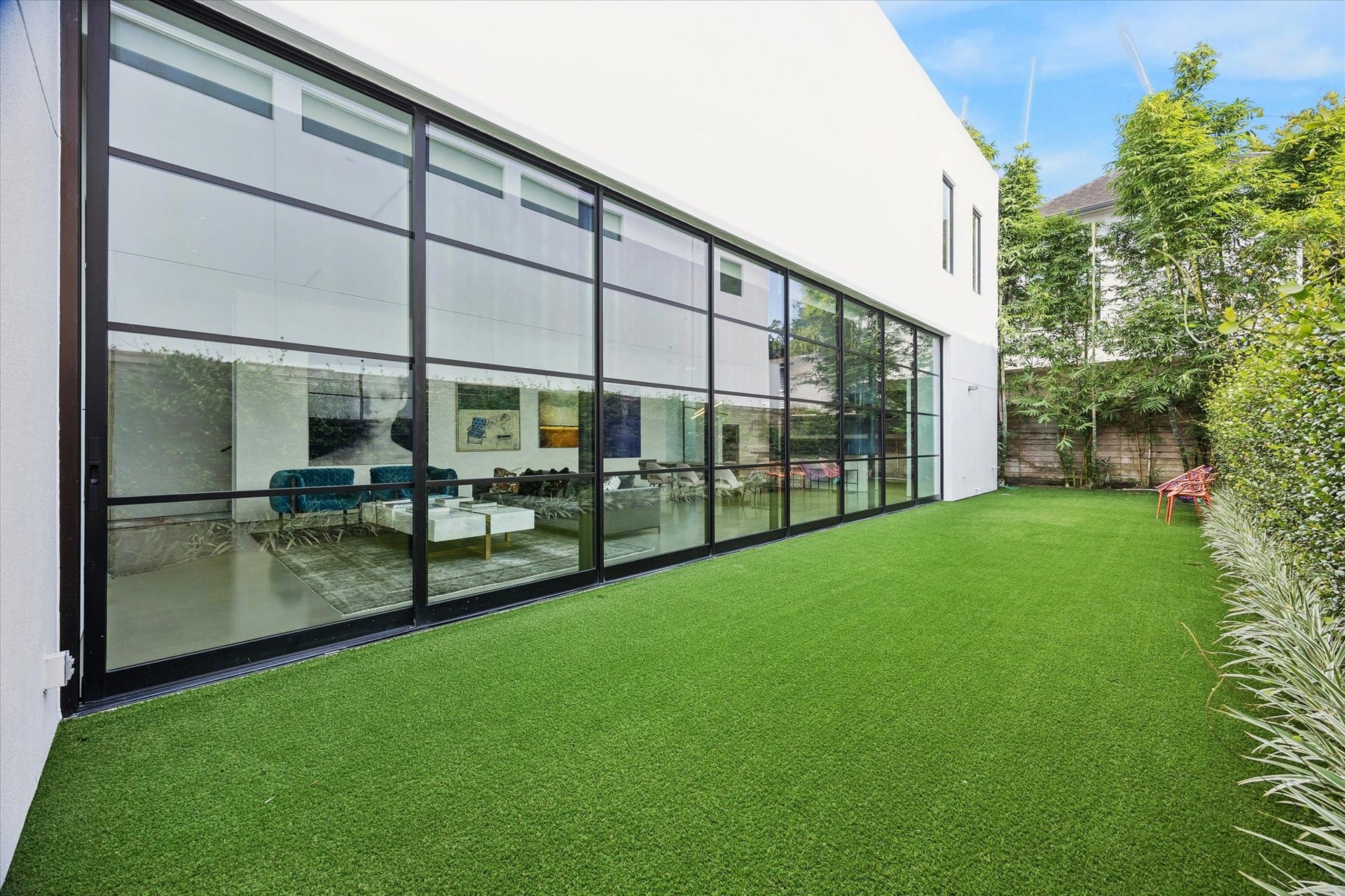 1527 Indiana Street, Houston, TX 77006 Serene outdoor retreat showcasing artificial turf and privacy-enhancing landscaping, while an expansive wall of floor-to-ceiling steel-framed windows creates a striking connection between the indoors and outdoors.