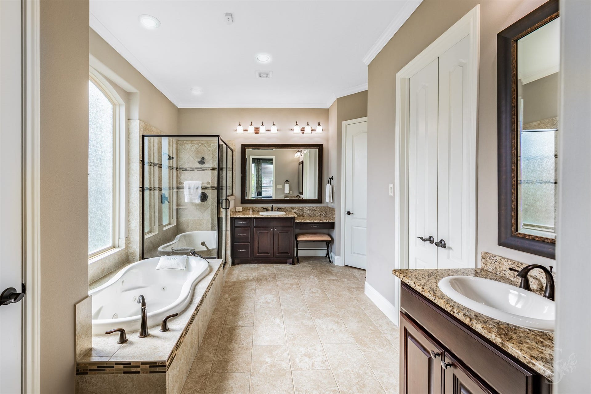 27506 Lakeway Trail Lane, Fulshear, TX 77441 Separate granite-topped vanities with richly stained cabinetry bring elegance and convenience to the spacious primary bath. A jetted tub beneath privacy windows and a separate glass-enclosed shower create an inviting retreat for unwinding.