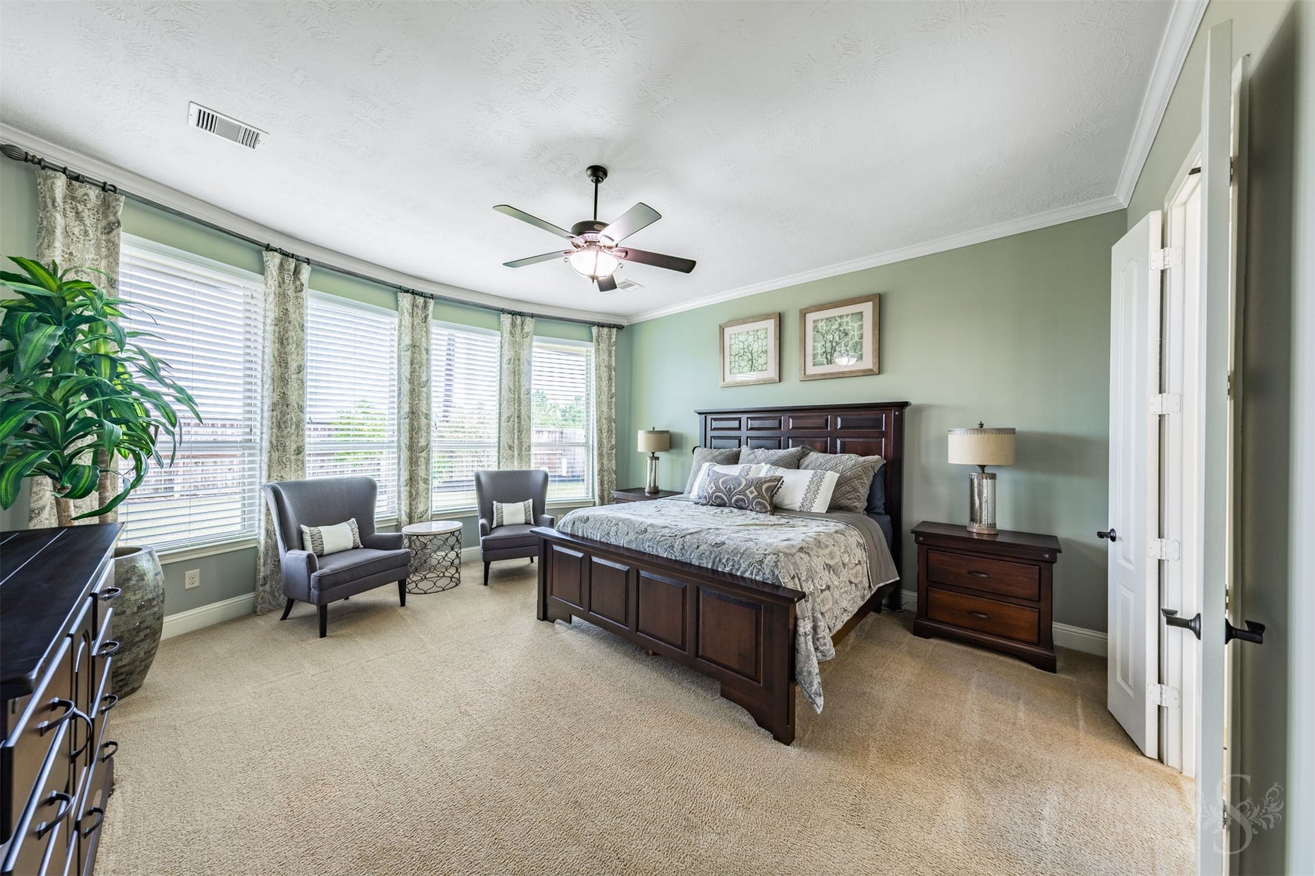 27506 Lakeway Trail Lane, Fulshear, TX 77441 The spacious primary bedroom offers a peaceful retreat with soft green walls, plush carpeting and elegant crown molding. A wall of tall windows brightens the room and provides a lovely backdrop for a comfortable sitting area.