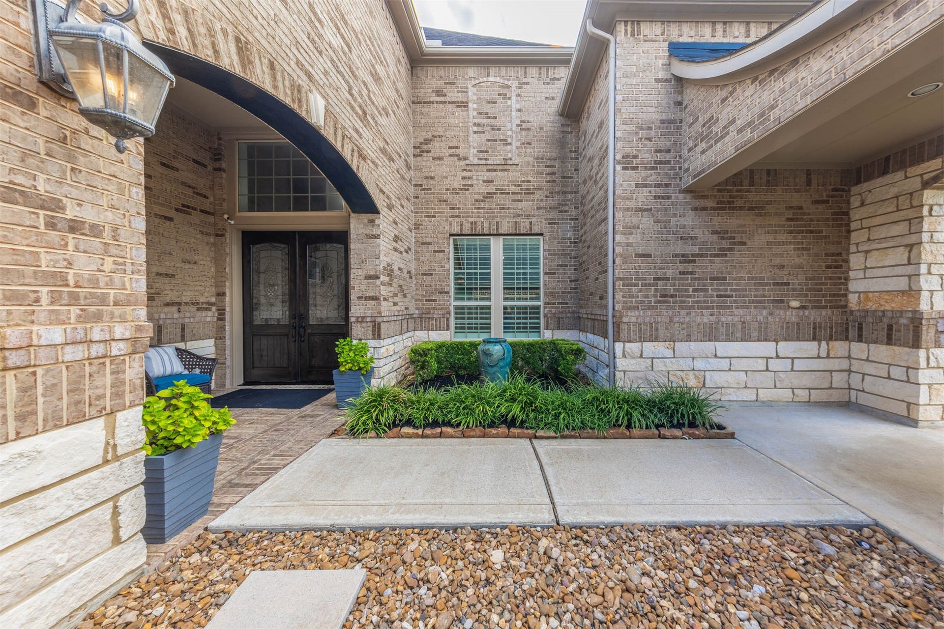 27506 Lakeway Trail Lane, Fulshear, TX 77441 An impressive brick arch frames the covered entrance, where richly stained double doors with decorative glass create an elegant welcome. Stone accents and lush landscaping add beautiful texture to the courtyard setting.