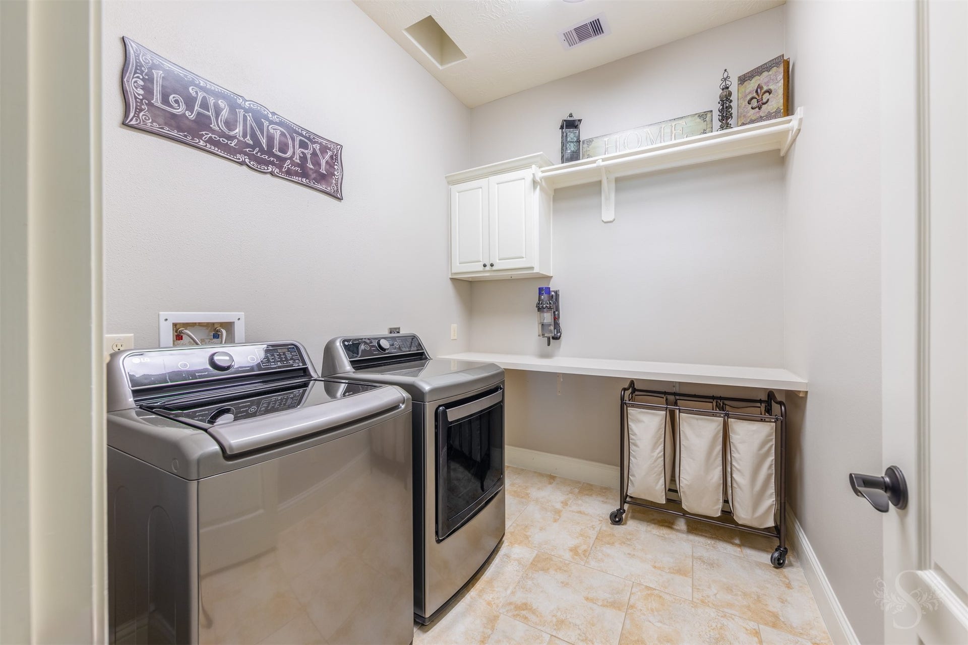27506 Lakeway Trail Lane, Fulshear, TX 77441 The spacious utility room features a long folding counter, white cabinetry and an overhead shelf with a hanging rod. Tile flooring and ample space for sorting laundry help keep daily routines organized.