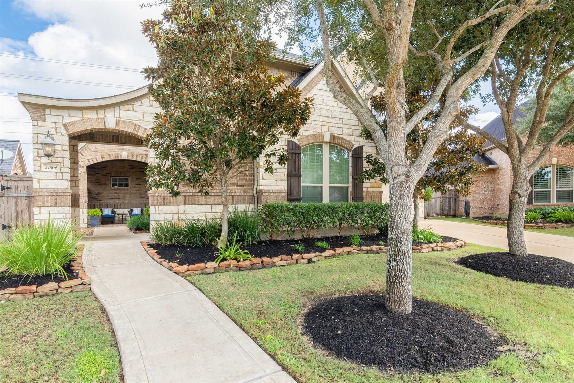 27506 Lakeway Trail Lane, Fulshear, TX 77441 A gently curved walkway leads past mature trees and beautifully landscaped beds to the striking arched courtyard entrance. The elegant blend of brick and stone creates a memorable welcome before you step inside.