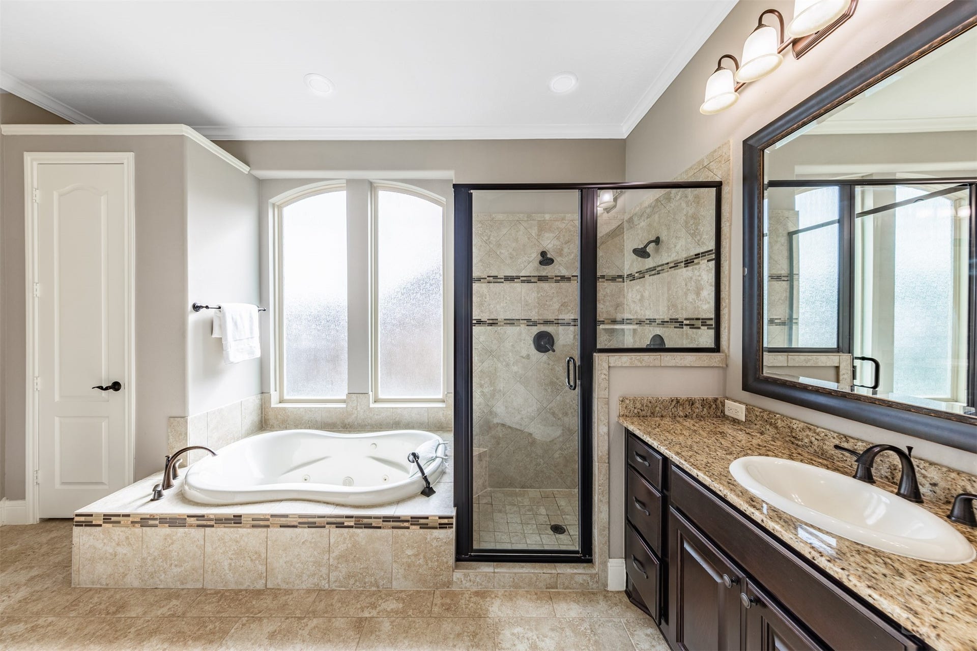 27506 Lakeway Trail Lane, Fulshear, TX 77441 Relax in the jetted tub beneath gracefully arched privacy windows, surrounded by warm tile and mosaic detailing. A separate shower with dual showerheads and a generous granite-topped vanity complete this luxurious retreat.