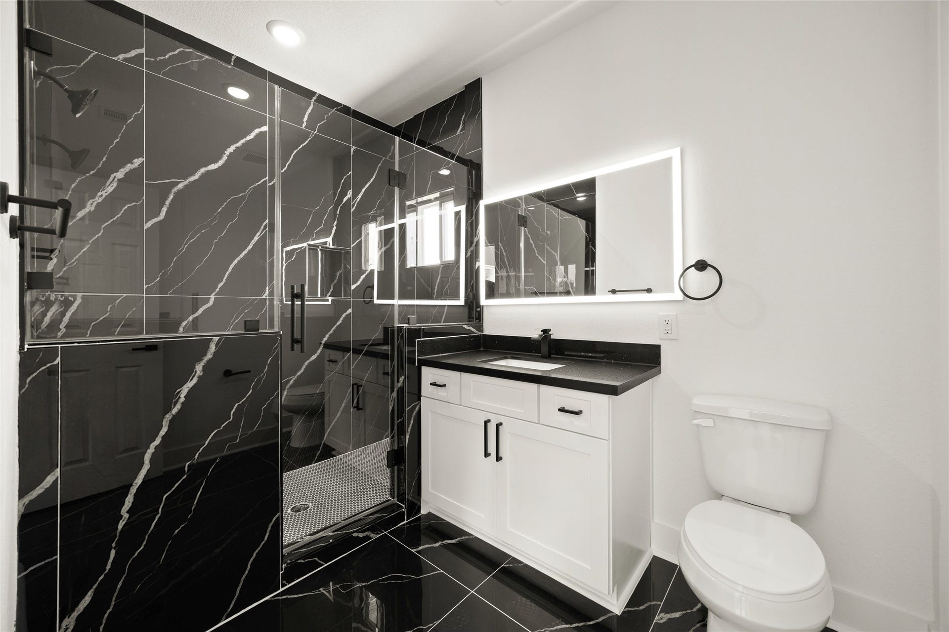 Luxurious bathroom featuring a striking black marble shower with white veining, complemented by a sleek vanity with an illuminated mirror.