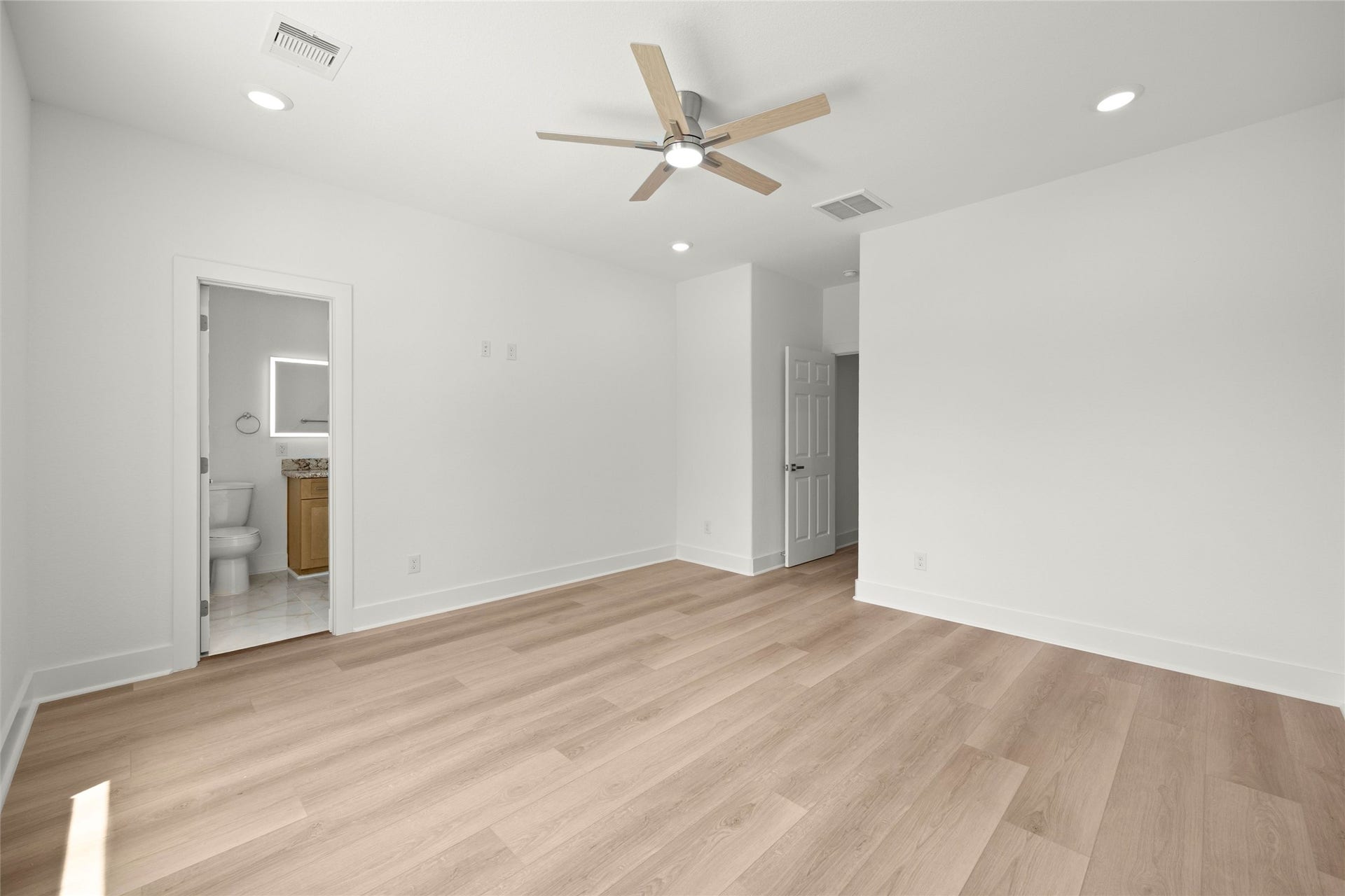 Spacious bedroom with sleek wood flooring, recessed lighting, and a ceiling fan, featuring an en-suite bathroom for added convenience.