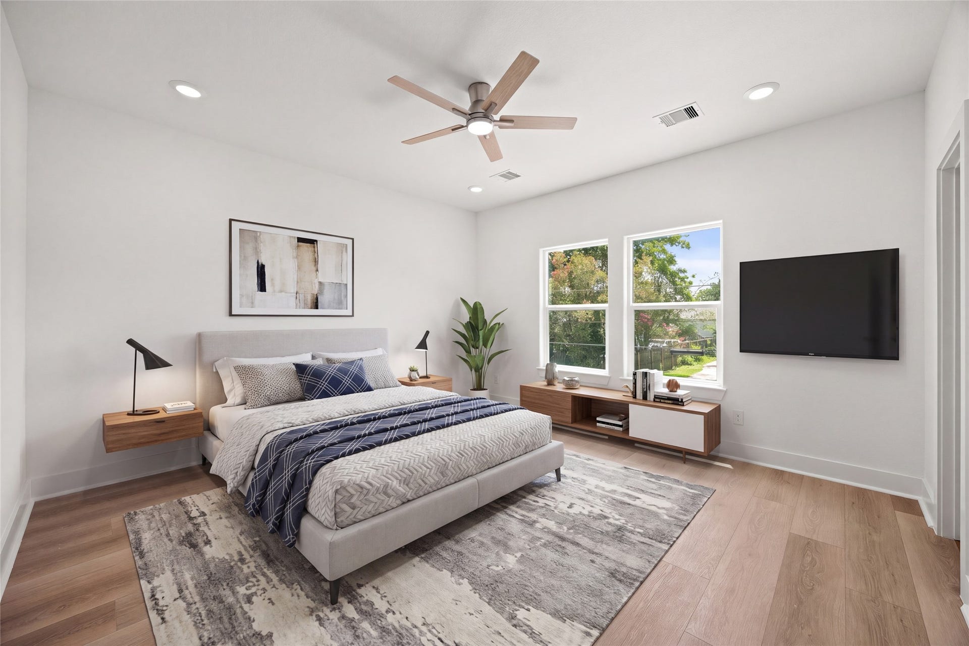 Bright and airy bedroom featuring large windows, sleek wood flooring, and a modern ceiling fan, offering a serene and inviting space.