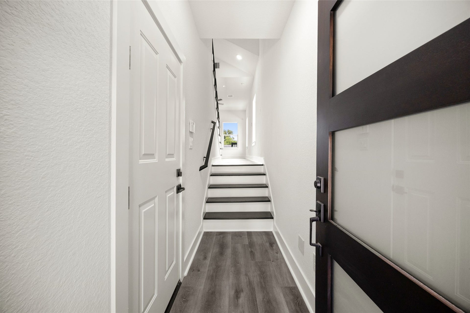 Bright and welcoming entryway with sleek flooring and a modern staircase leading to the main living area, offering a glimpse of the outdoors.