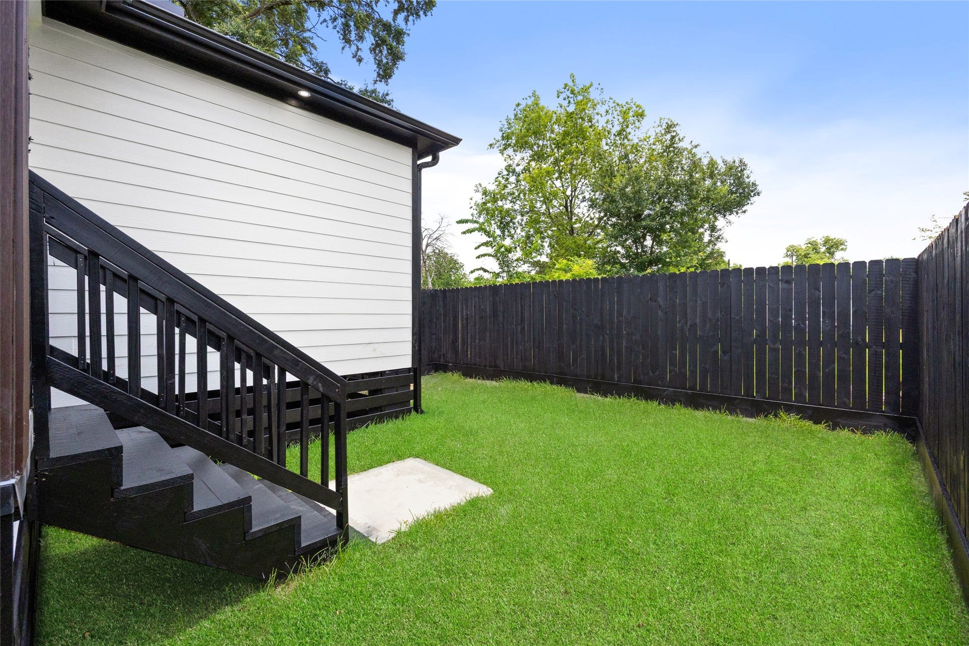 Charming backyard with lush green grass, a sleek black fence for privacy, and a convenient stairway leading to the home.
