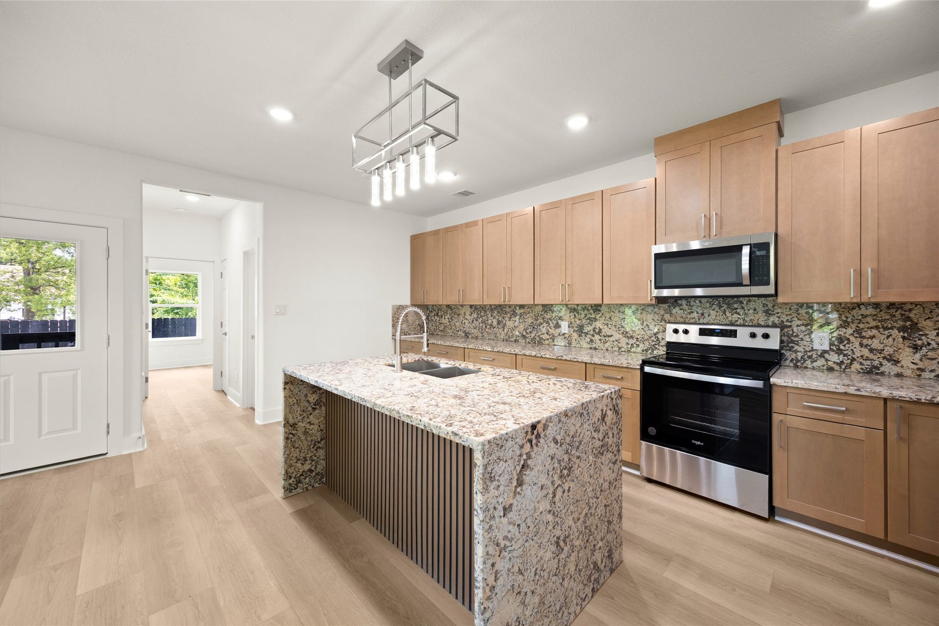 Modern kitchen featuring a spacious granite island, sleek stainless steel appliances, and ample light wood cabinetry for a stylish and functional cooking space.