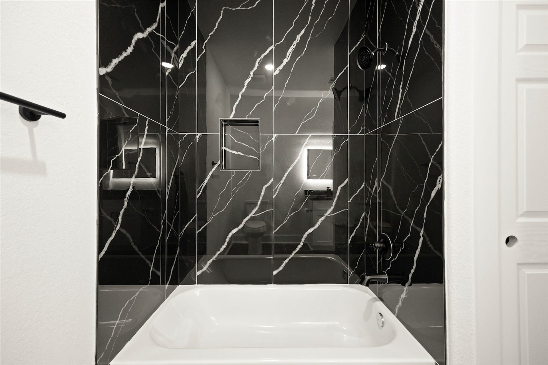 Elegant bathroom featuring a sleek black marble shower with stunning white veining, complemented by a modern white bathtub.