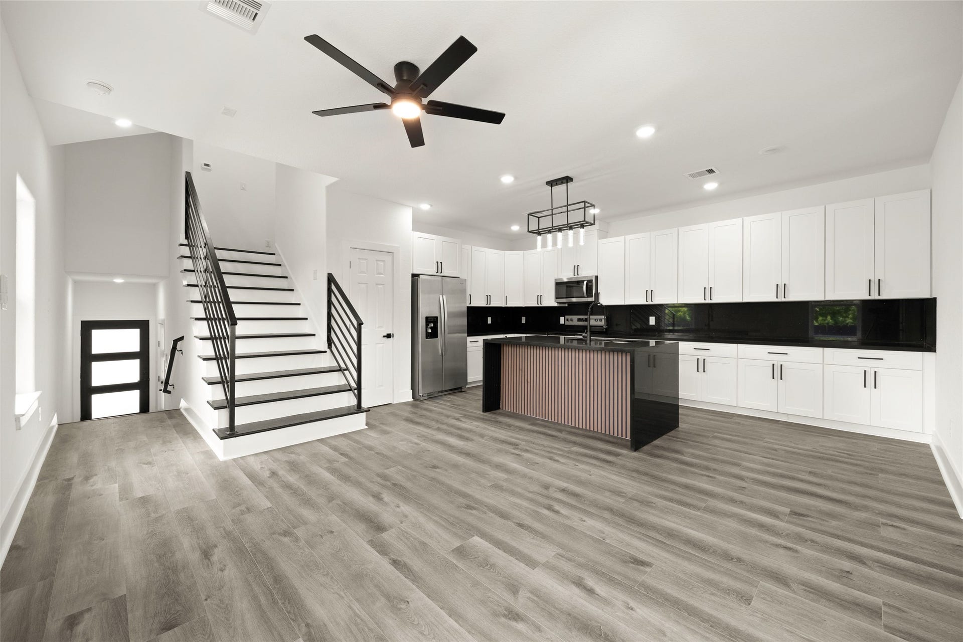 Sleek modern kitchen with stainless steel appliances, expansive white cabinetry, and a stylish island. The open layout features elegant flooring and a contemporary staircase, creating a perfect blend of style and functionality.