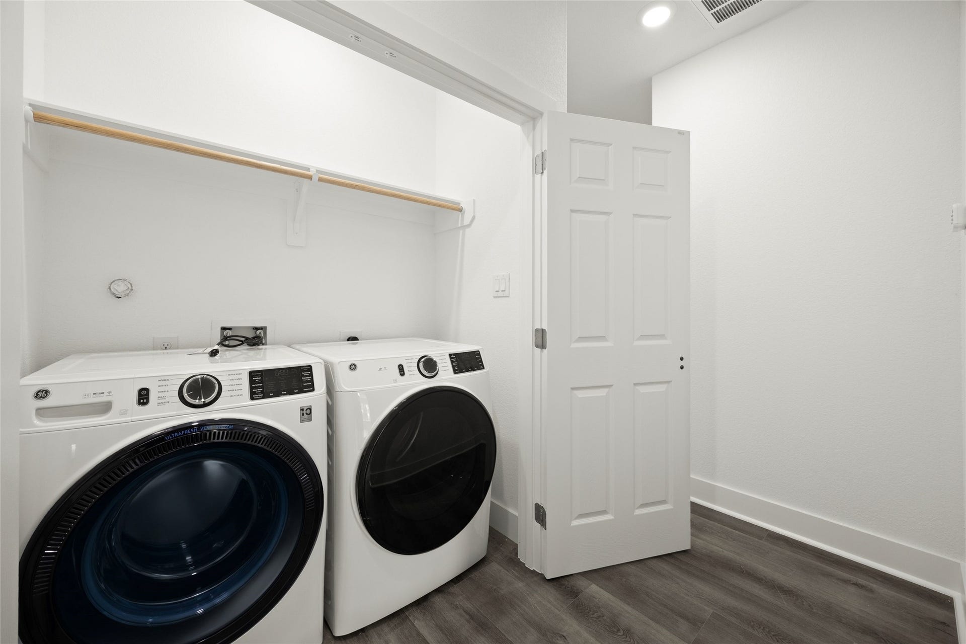 Modern laundry room with sleek front-loading washer and dryer, featuring ample shelving for storage and stylish wood-look flooring.