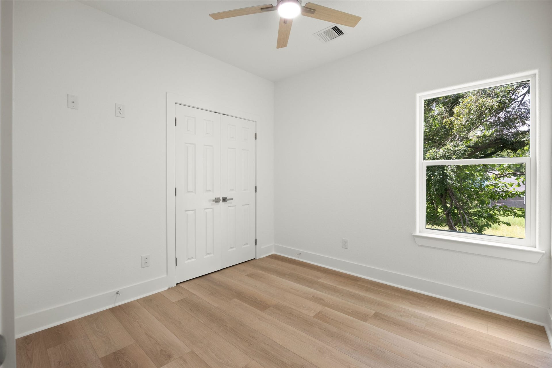 Bright and airy room featuring elegant wood flooring, a ceiling fan for comfort, and a large window inviting in natural light with views of lush greenery.