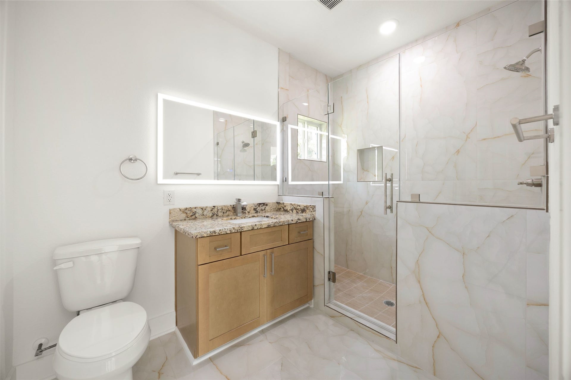 Elegant bathroom featuring a spacious glass-enclosed shower with luxurious marble-style tiles, complemented by a modern vanity with granite countertops and a sleek illuminated mirror.