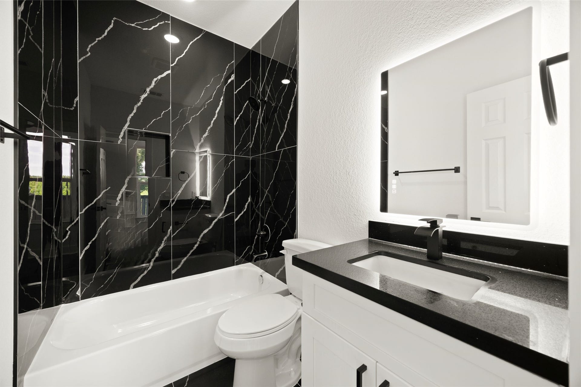 Sleek bathroom featuring striking black marble tiles, a modern LED-lit mirror, and a stylish black countertop for a luxurious touch.