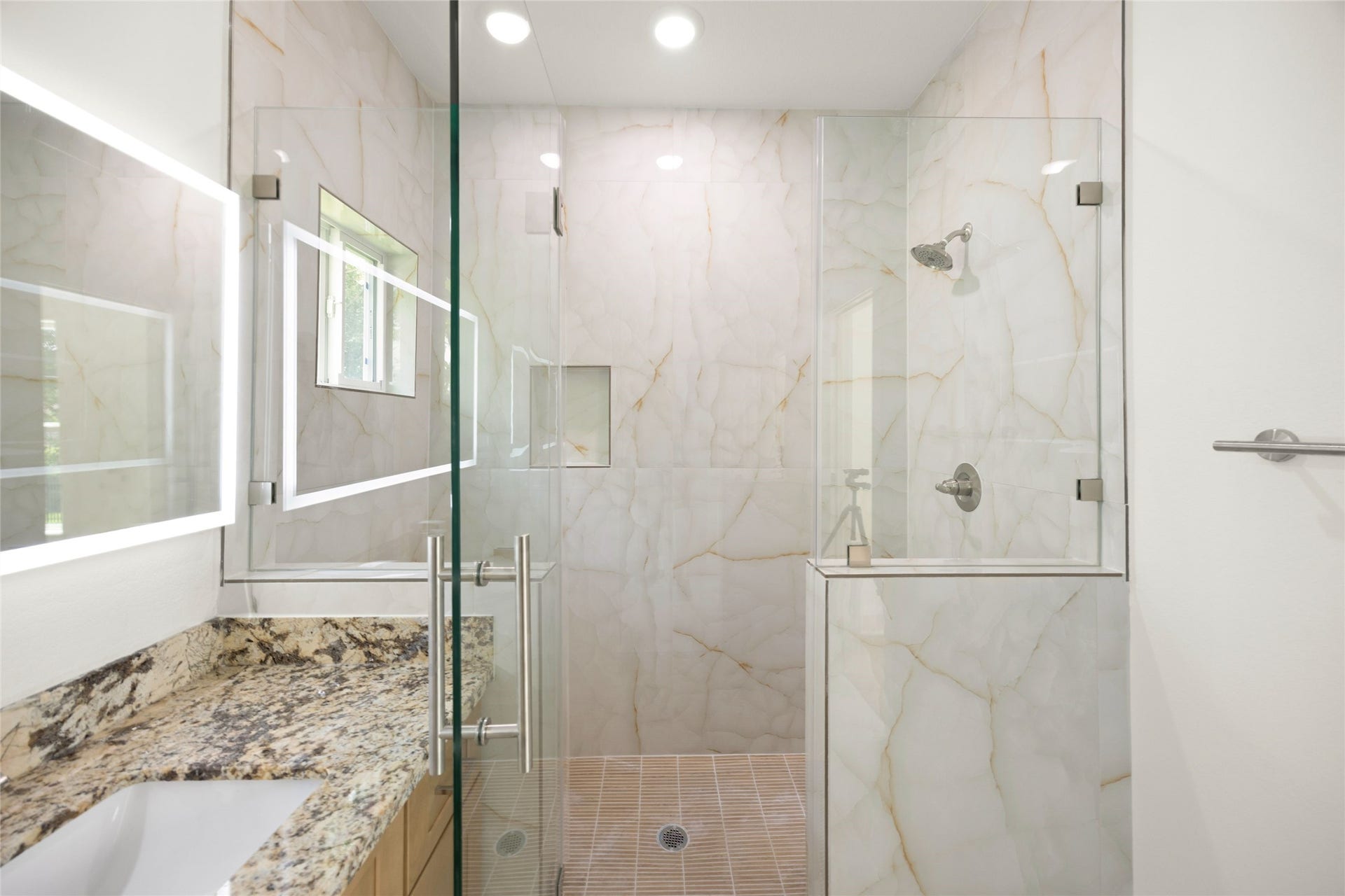 Elegant bathroom featuring a spacious glass-enclosed shower with luxurious marble walls, complemented by a sleek granite countertop.