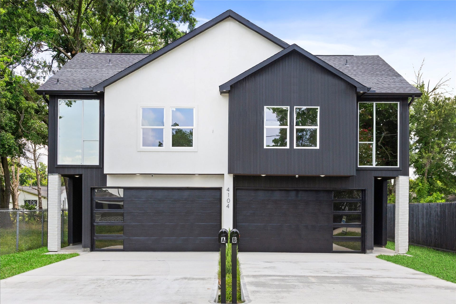 Modern duplex featuring sleek black and white exterior, expansive windows, and dual garage doors, set on a spacious driveway.