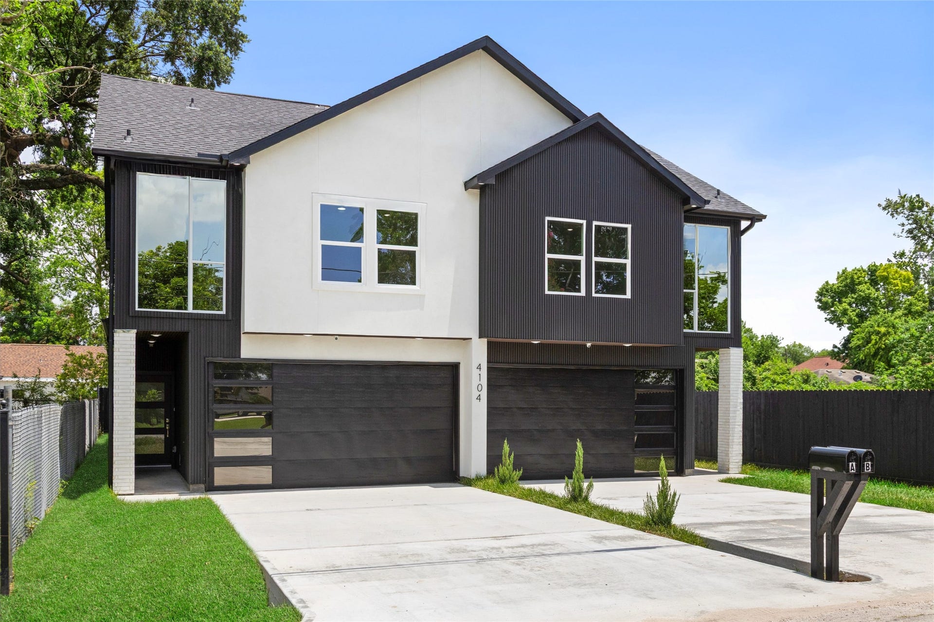 Modern duplex with sleek black and white facade, large windows, and spacious double garage, nestled in a serene neighborhood.