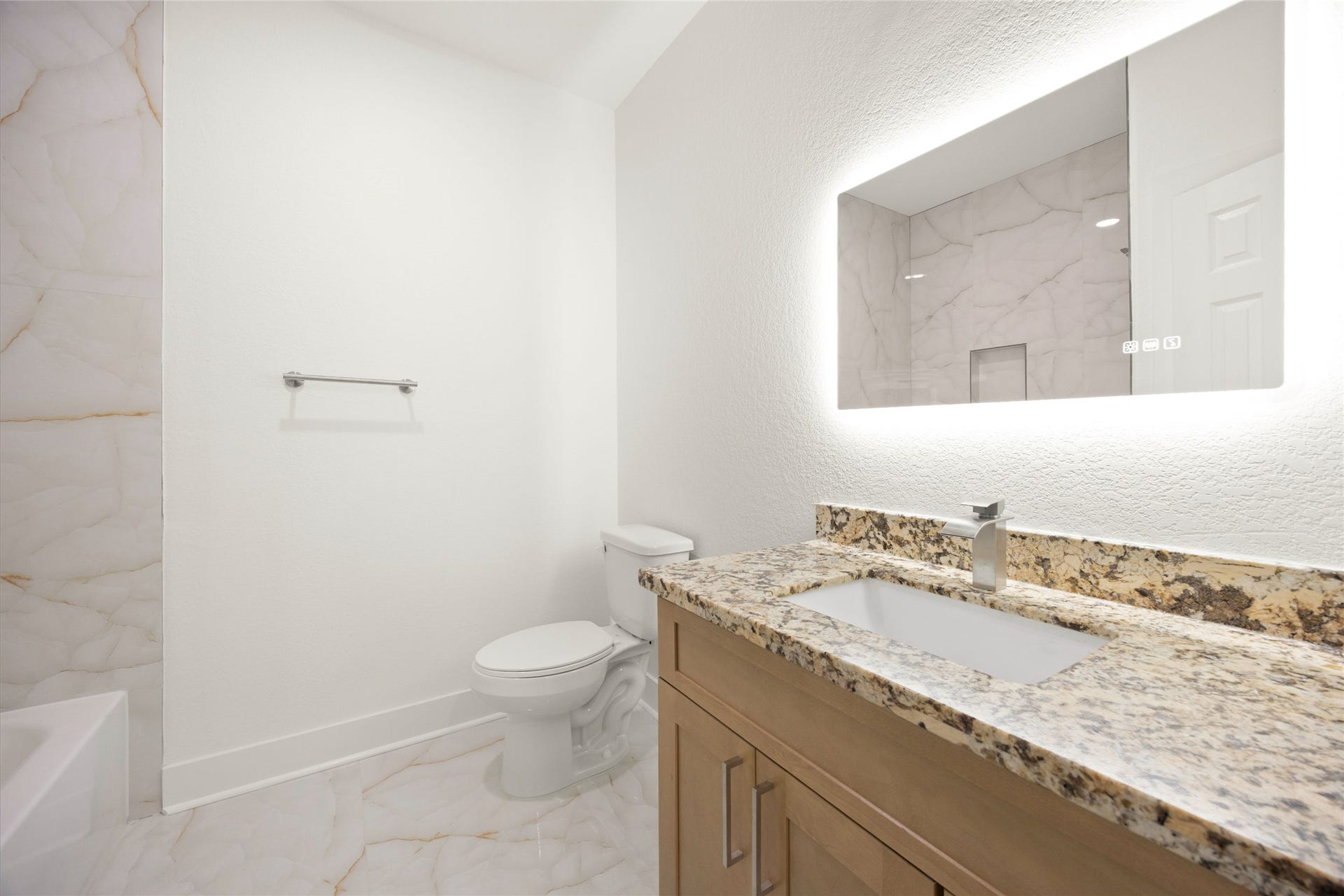 Elegant bathroom featuring a sleek granite countertop, modern sink, and an illuminated mirror, complemented by luxurious marble flooring and shower walls.