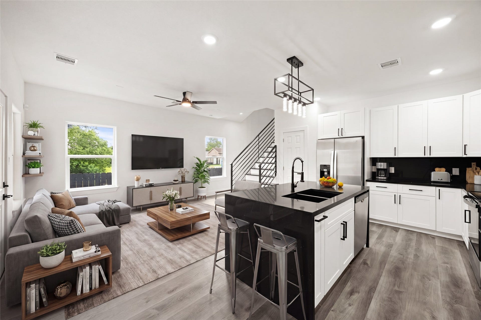 Modern open-concept living space with sleek black countertops, stainless steel appliances, and elegant white cabinetry, complemented by stylish lighting and a contemporary staircase.