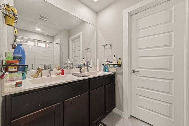 7523 Keystone Blossom Trail, Richmond, TX 77407 Primary bathroom featuring a dual-sink vanity with extended counter space, complemented by a large mirror and a separate glass-enclosed shower with tiled surround.
