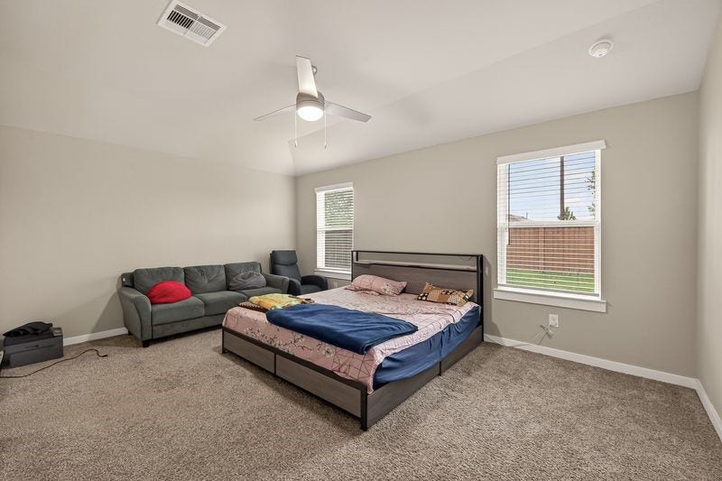 7523 Keystone Blossom Trail, Richmond, TX 77407 Spacious primary bedroom featuring soft carpeting, dual windows for natural light, and a ceiling fan centered within an open, airy layout.