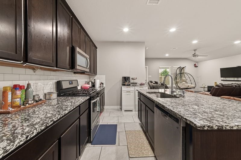 7523 Keystone Blossom Trail, Richmond, TX 77407 Well-appointed kitchen featuring granite countertops, dark cabinetry, stainless steel appliances, and a central island with an integrated sink overlooking the living area.